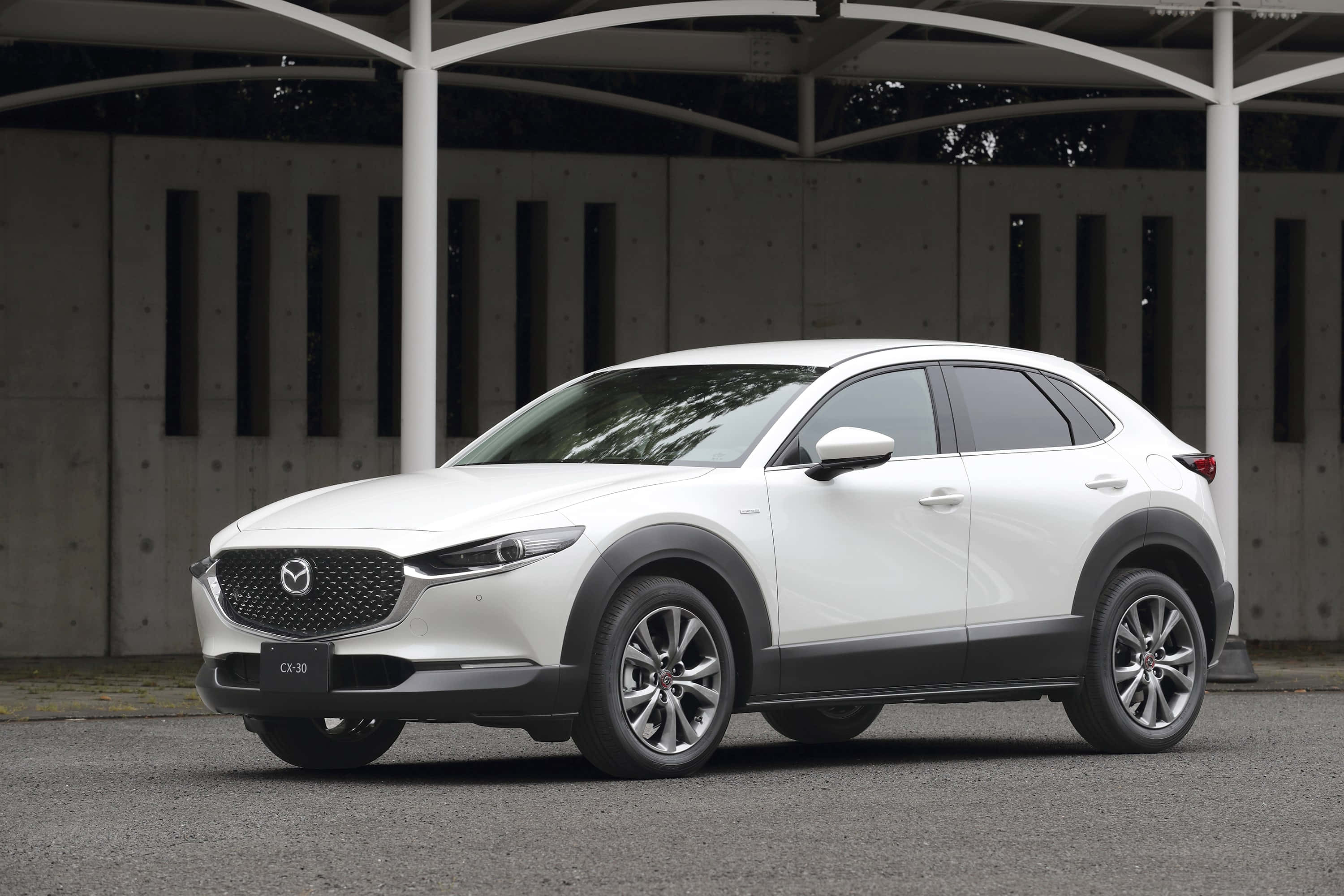 Mazda Cx-30 桌布 壁紙 — 一輛時尚的白色Mazda CX-30 SUV停放在帶有混凝土牆的現代金屬簷篷下。