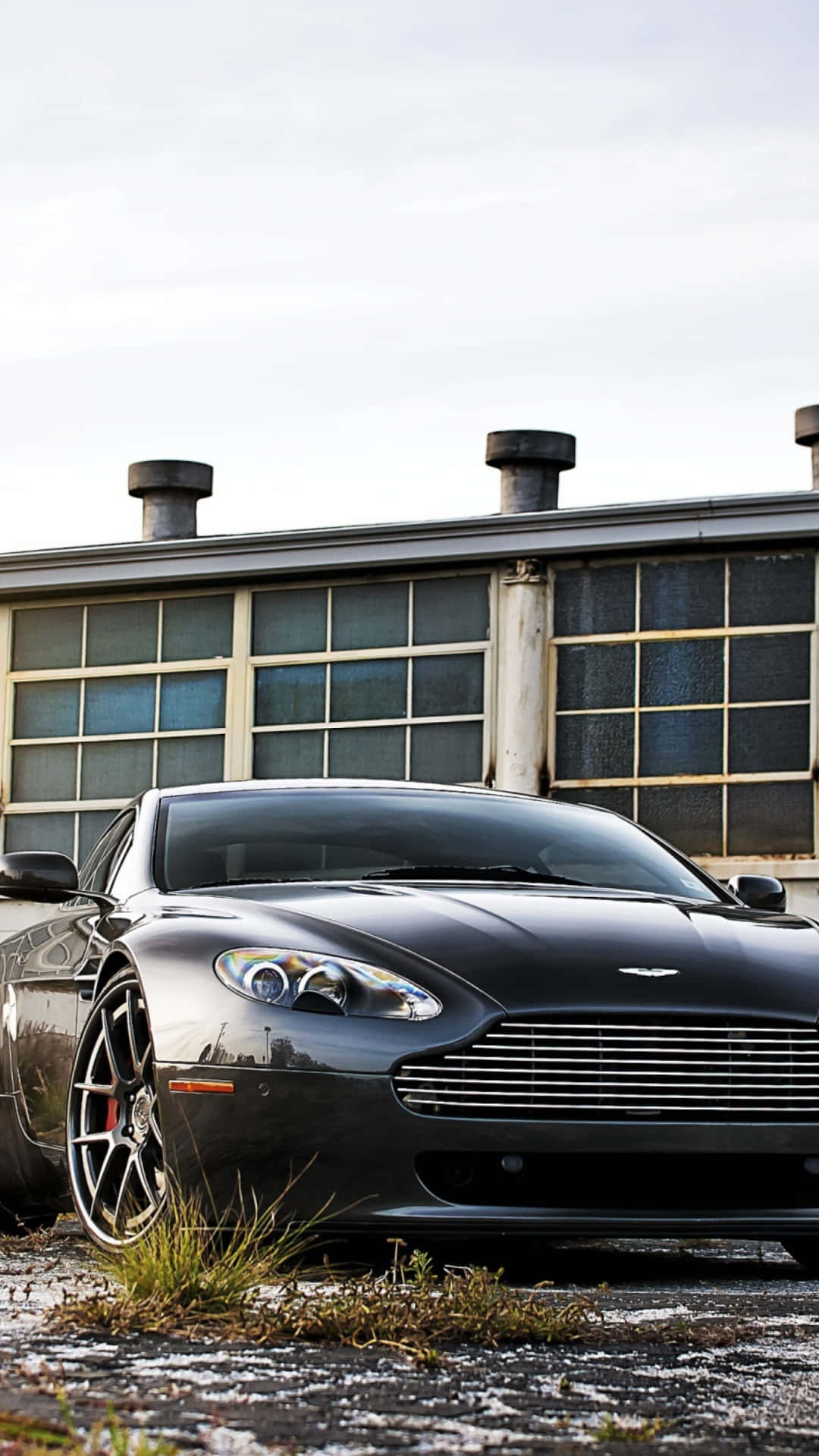 Aston Martin Vantage 桌布 壁紙 — 一輛時尚的黑色Aston Martin跑車停在風化的工業建築前，地面有積雪。