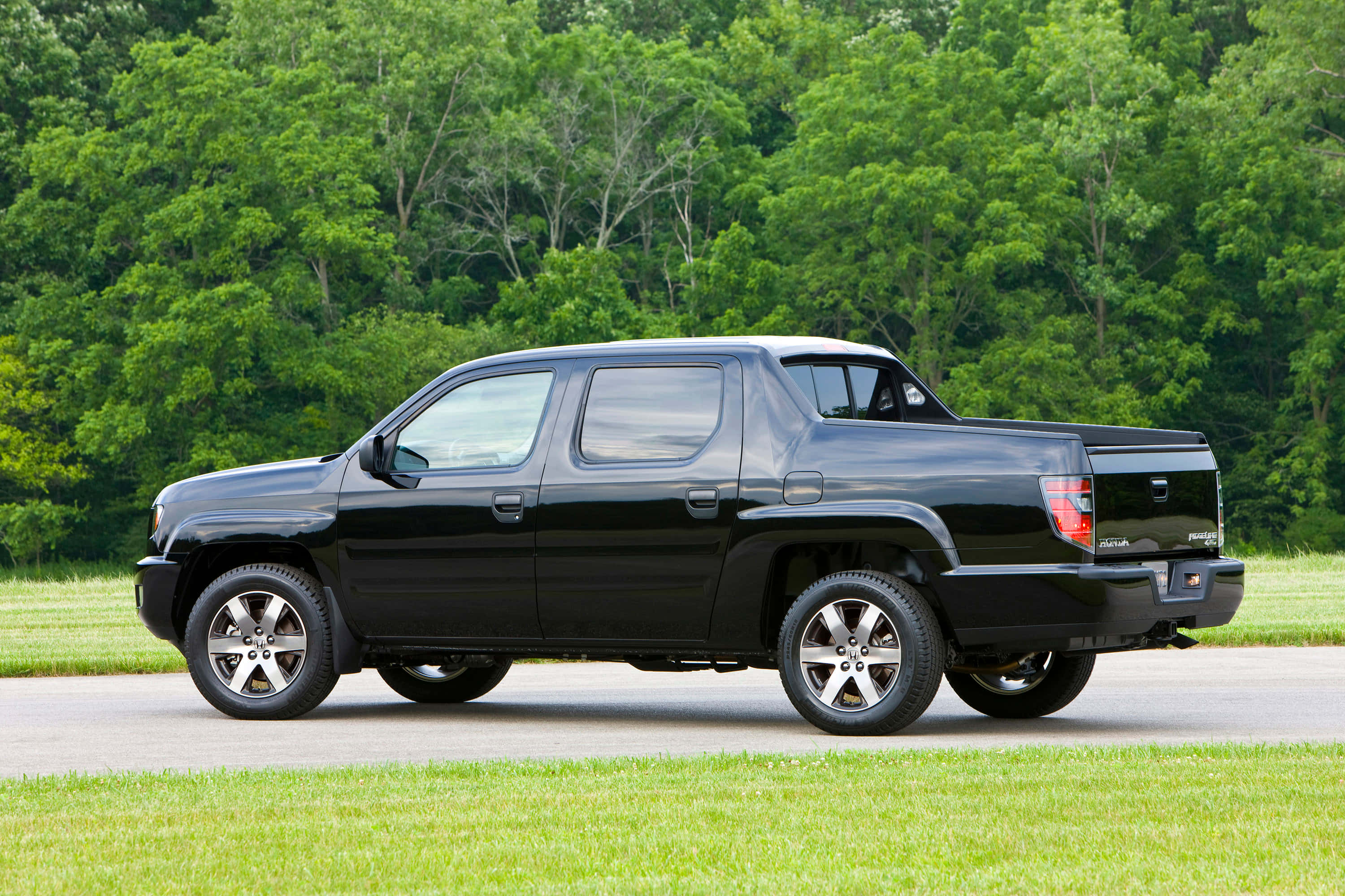 Honda Ridgeline 桌布 壁紙 — 一輛時尚的黑色本田 Ridgeline 皮卡車停在鋪砌的道路上，背景是茂密的綠樹和草地。