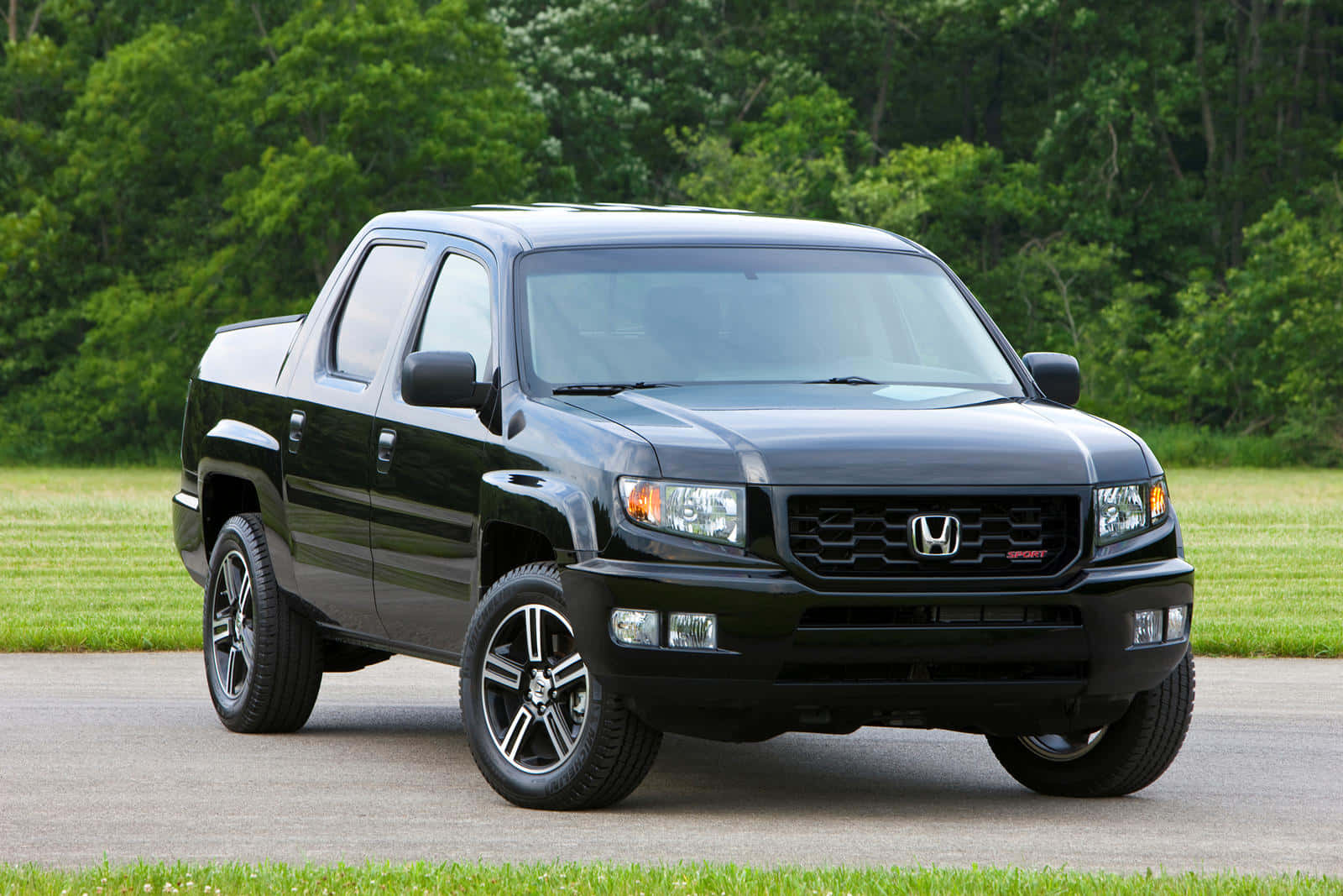 Honda Ridgeline 桌布 壁紙 — 一輛時尚的黑色本田Ridgeline皮卡車停在鋪砌的小路上，背景是茂密的綠色草地和茂密的森林。