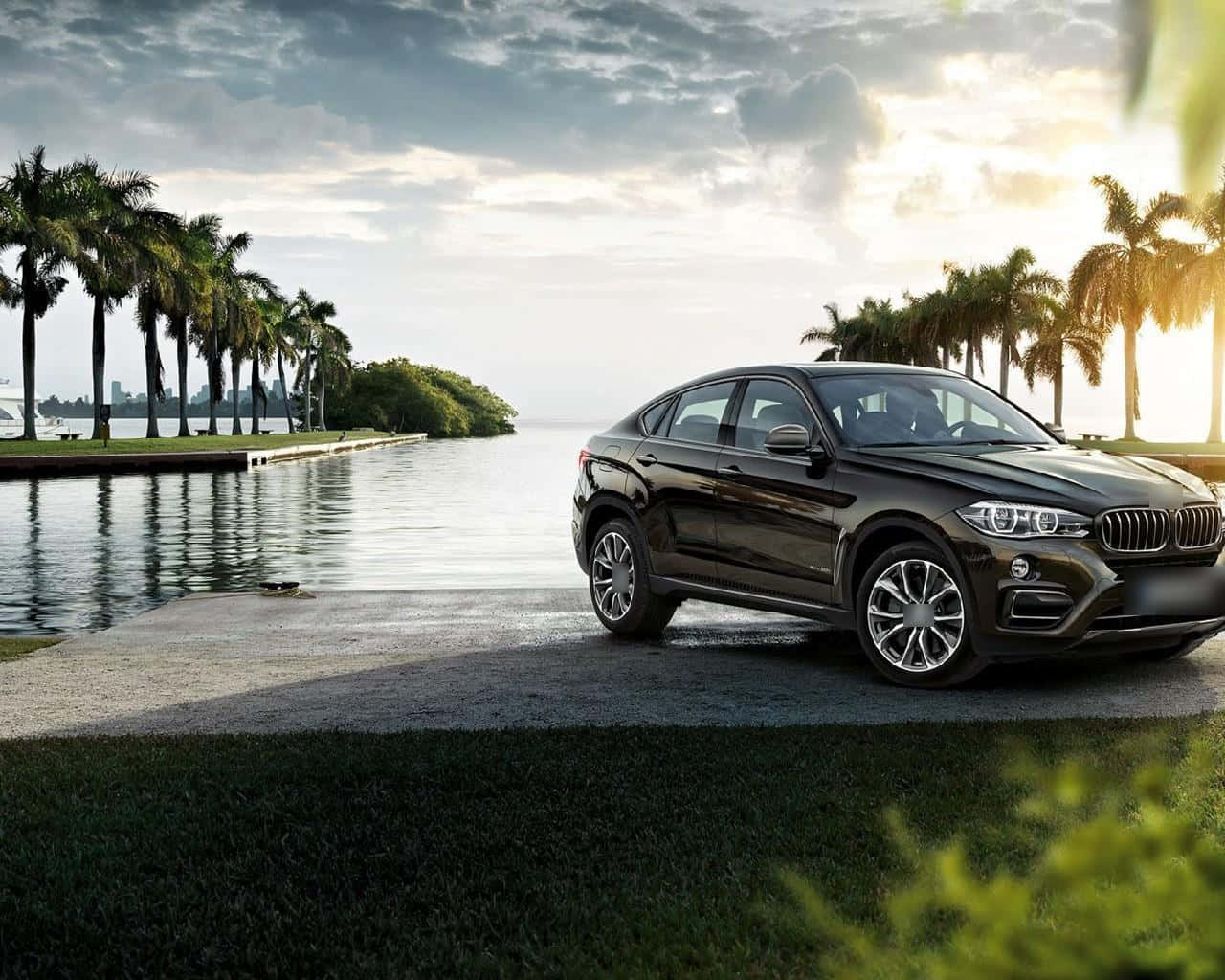 Bmw X6 桌布 壁紙 — 一輛時尚的黑色BMW X6停在海濱，棕櫚樹和日落時多雲的天空。