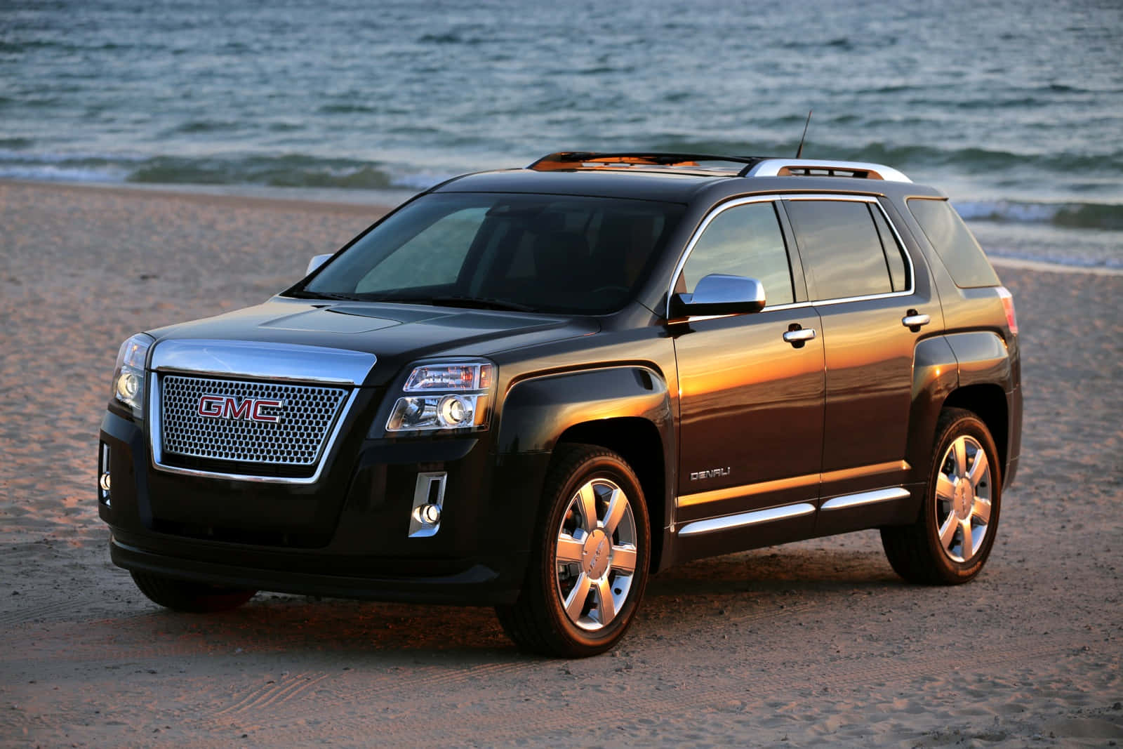 Gmc Terrain 桌布 壁紙 — 一輛時尚的黑色GMC Acadia SUV停泊在沙灘上，背景是黃金時段的海浪。