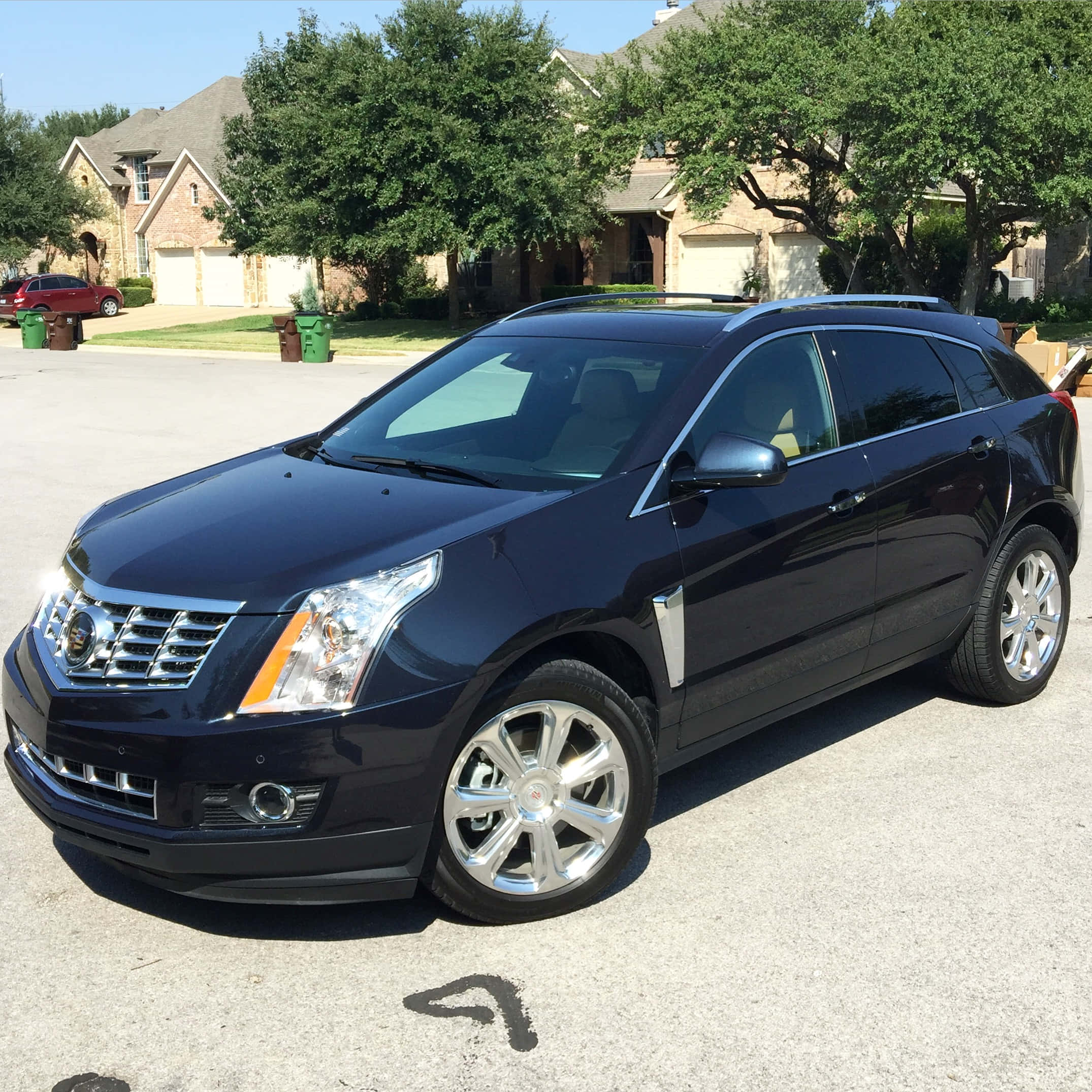 Cadillac Srx 桌布 壁紙 — 一輛時尚的黑色凱迪拉克 SRX SUV 停放在陽光明媚的郊區車道上，背景是磚房和綠樹。