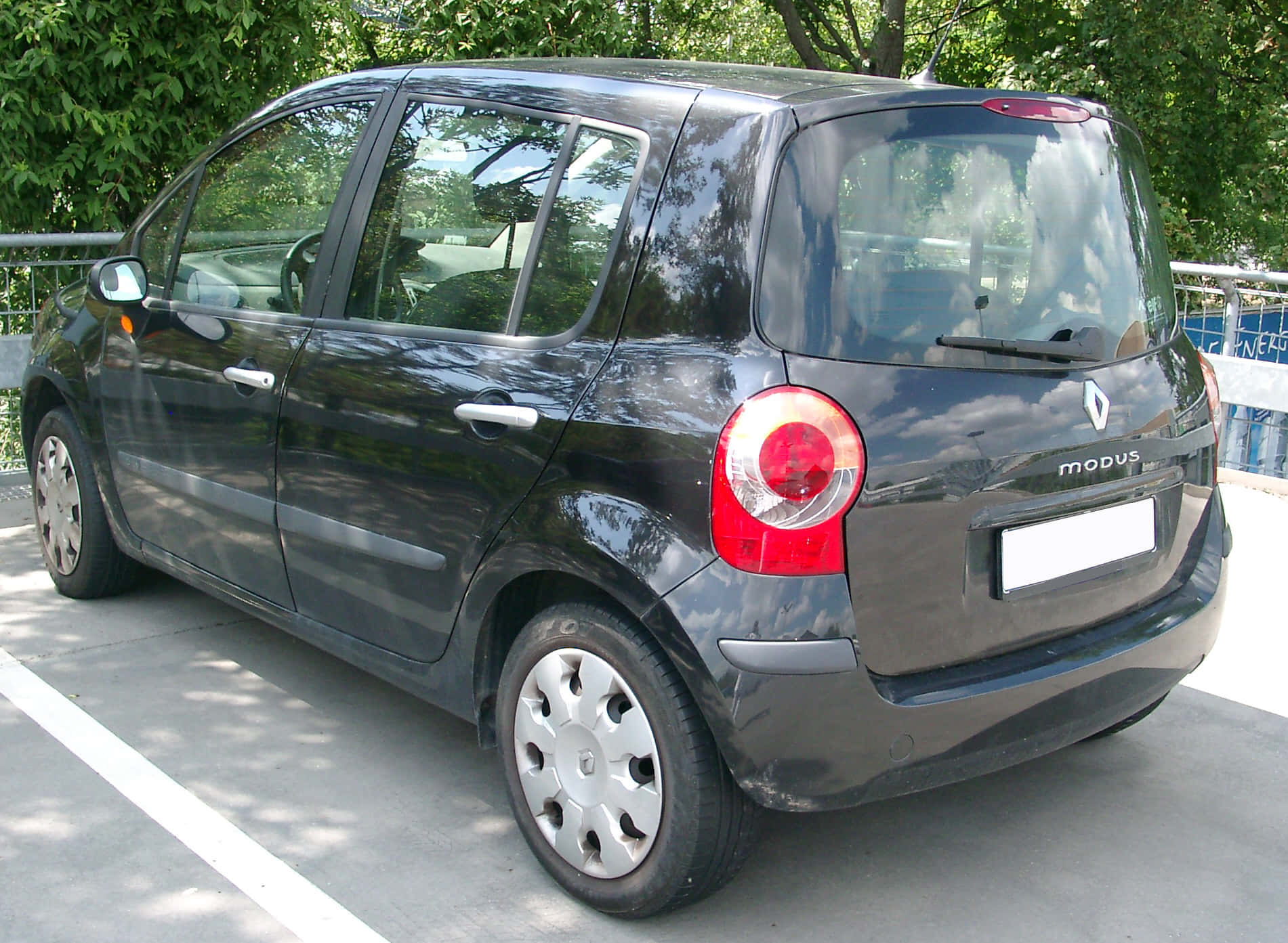 Renault Modus 桌布 壁紙 — 一輛時尚的黑色雷諾Modus停放在陽光普照的停車場，綠色樹木在其光澤表面反射。