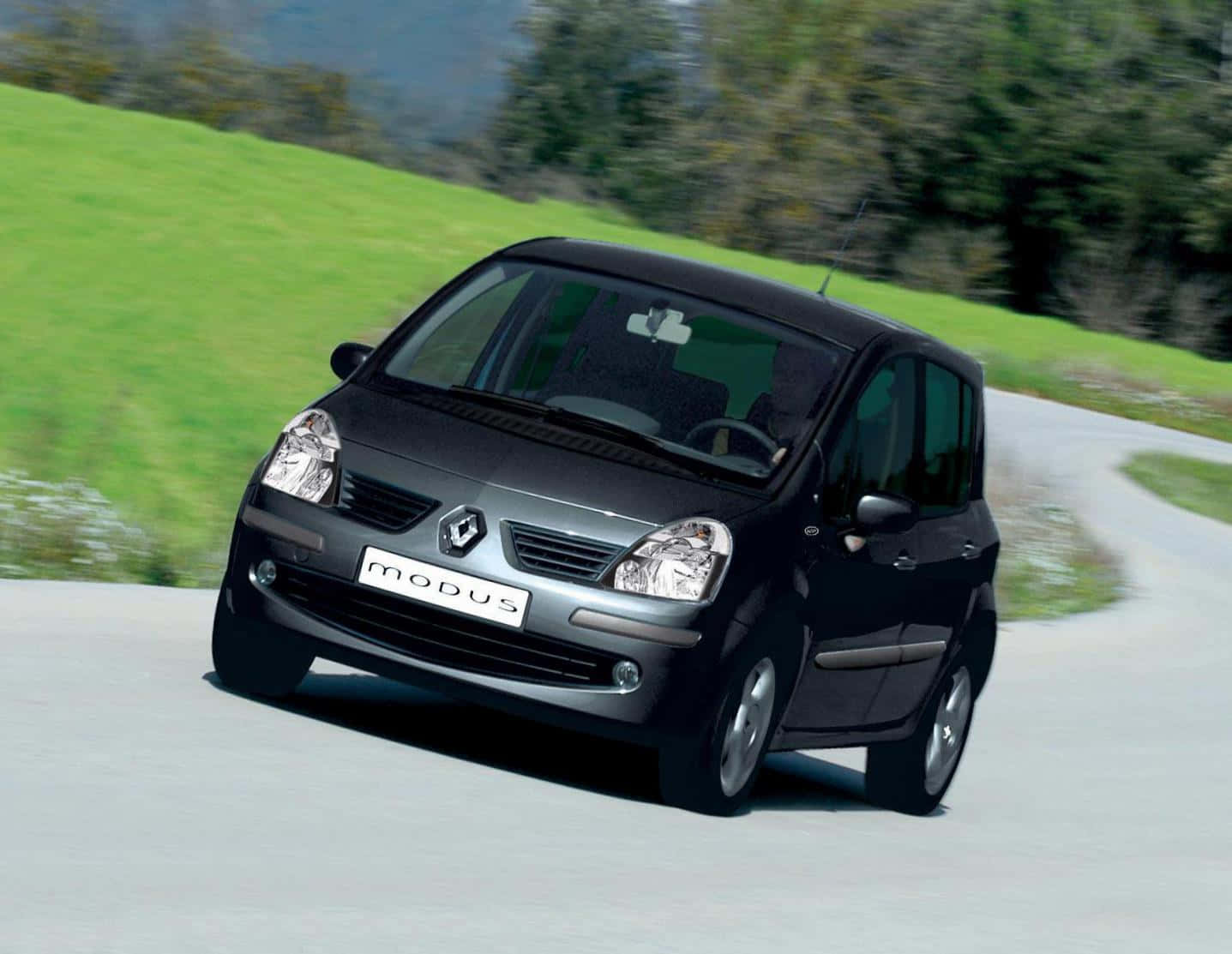 Renault Modus 桌布 壁紙 — 一輛時尚的黑色雷諾Modus在明亮的日光下行駛在蜿蜒的道路上，穿過鬱鬱蔥蔥的綠色山丘。