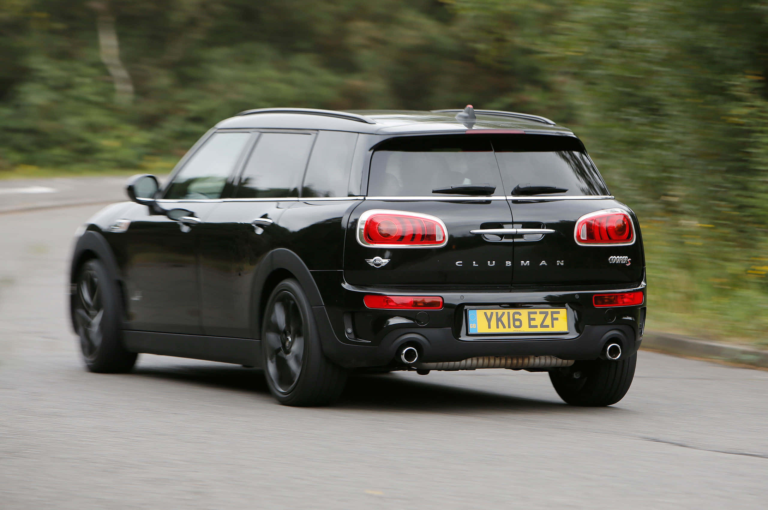 Mini Cooper S Clubman All4 桌布 壁紙 — 一輛時尚的黑色Mini Clubman在綠樹成蔭的道路上行駛，動態模糊傳達出速度與優雅。