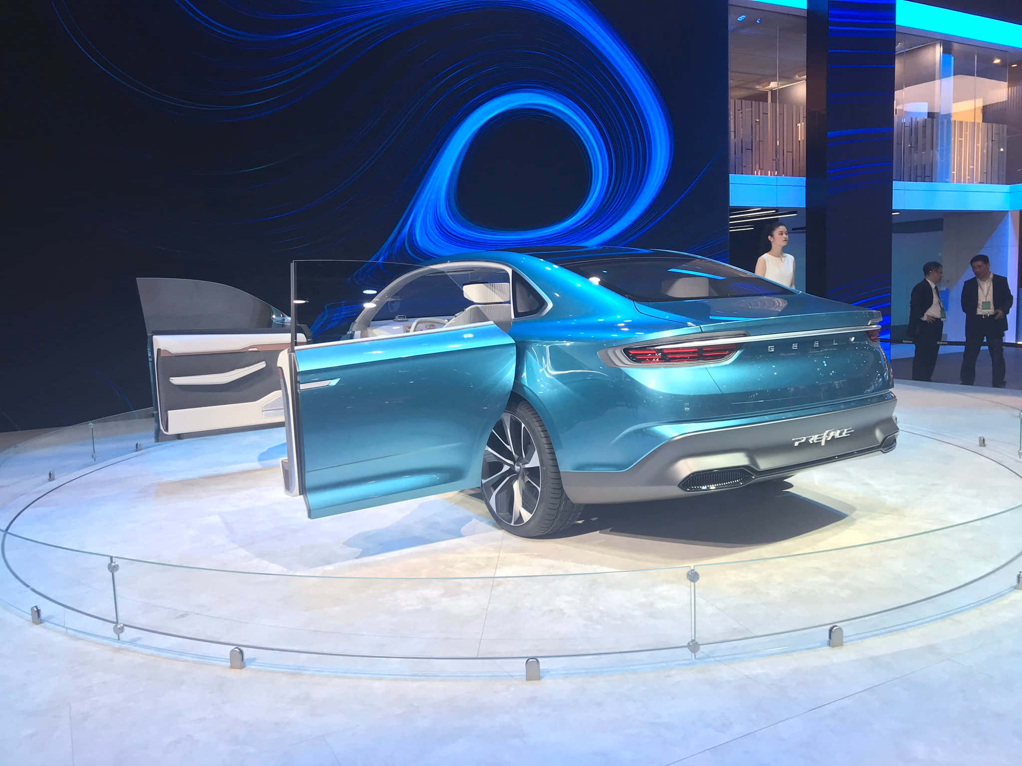 Geely Preface 桌布 壁紙 — 一輛時尚的藍綠色概念車，車門敞開，在旋轉的藍色燈光裝置下的圓形平台上展示。