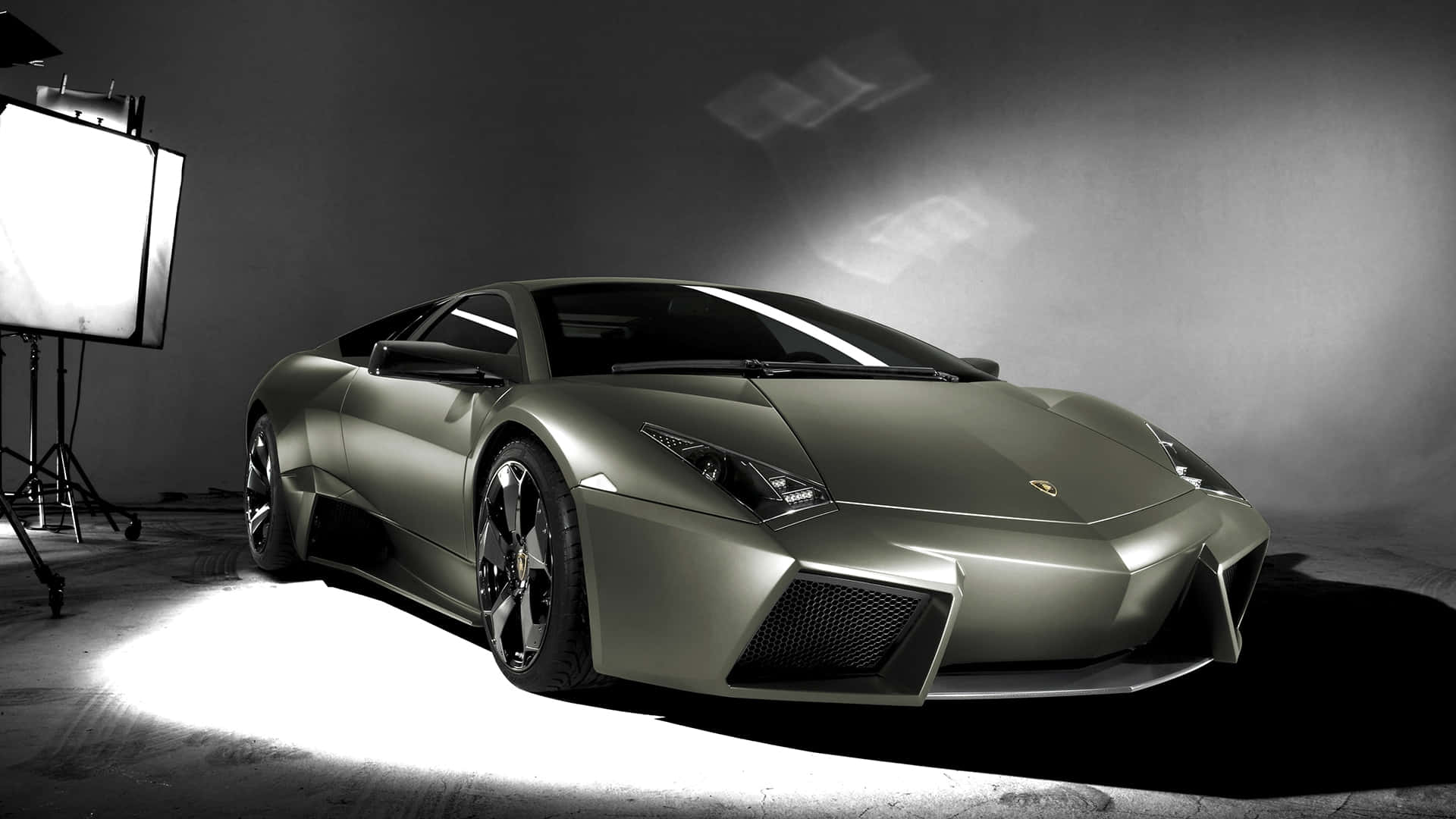 Lamborghini Reventón 桌布 壁紙 — 一輛時尚的啞光綠色林寶堅尼跑車在攝影棚內被戲劇性地照亮，可見的照明設備投射出銳利的陰影。