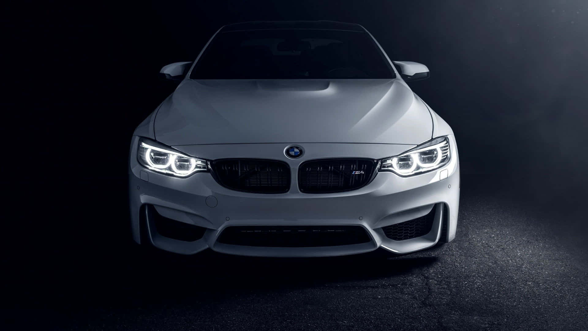 在黑暗的攝影棚中，銀色BMW M4跑車的前視圖，頭燈發光。