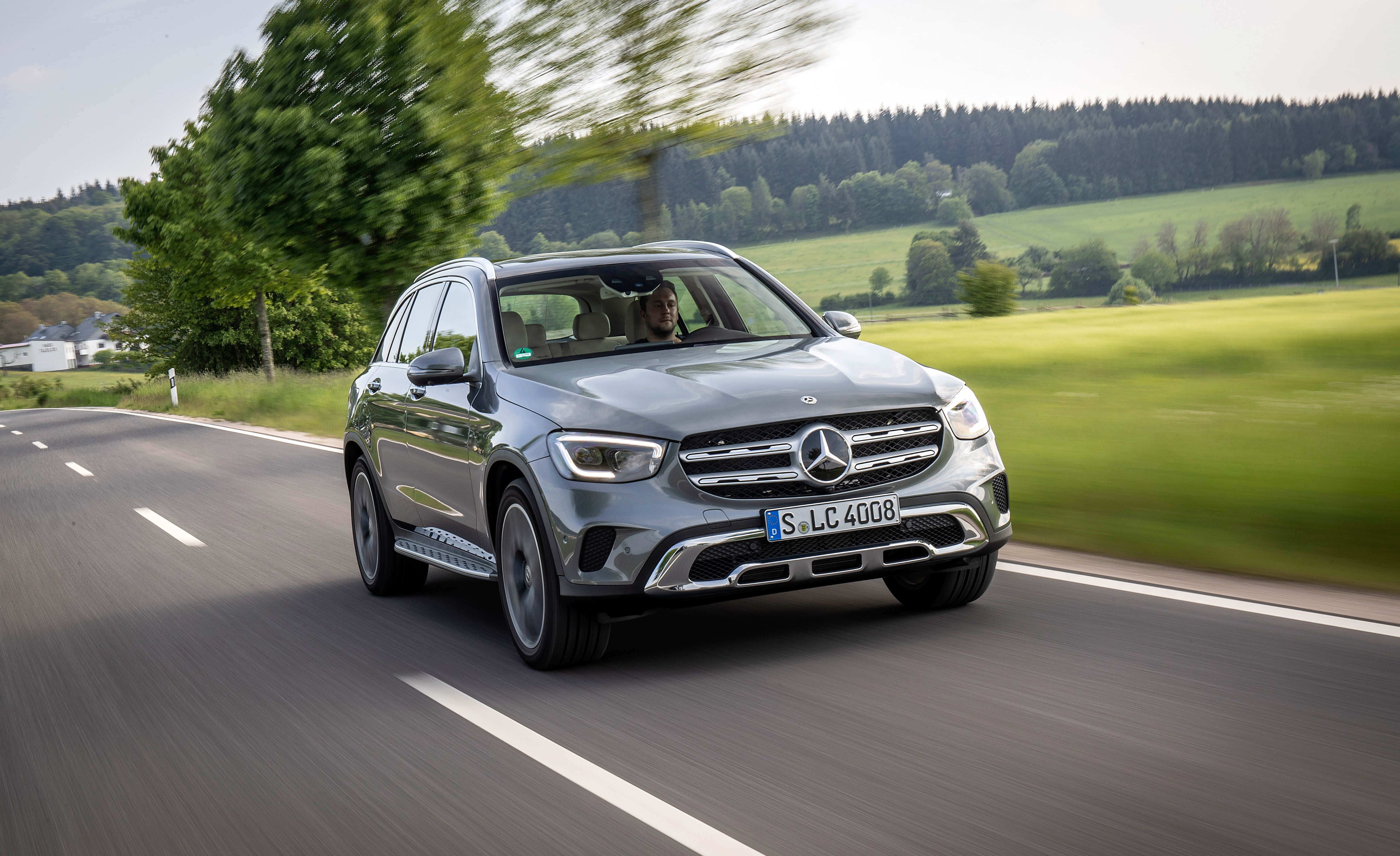 Mercedes Benz Glc-class 桌布 壁紙 — 一輛時尚的銀色 Mercedes GLC SUV 在蜿蜒的鄉村道路上疾馳，背景是模糊的綠色田野和樹木。