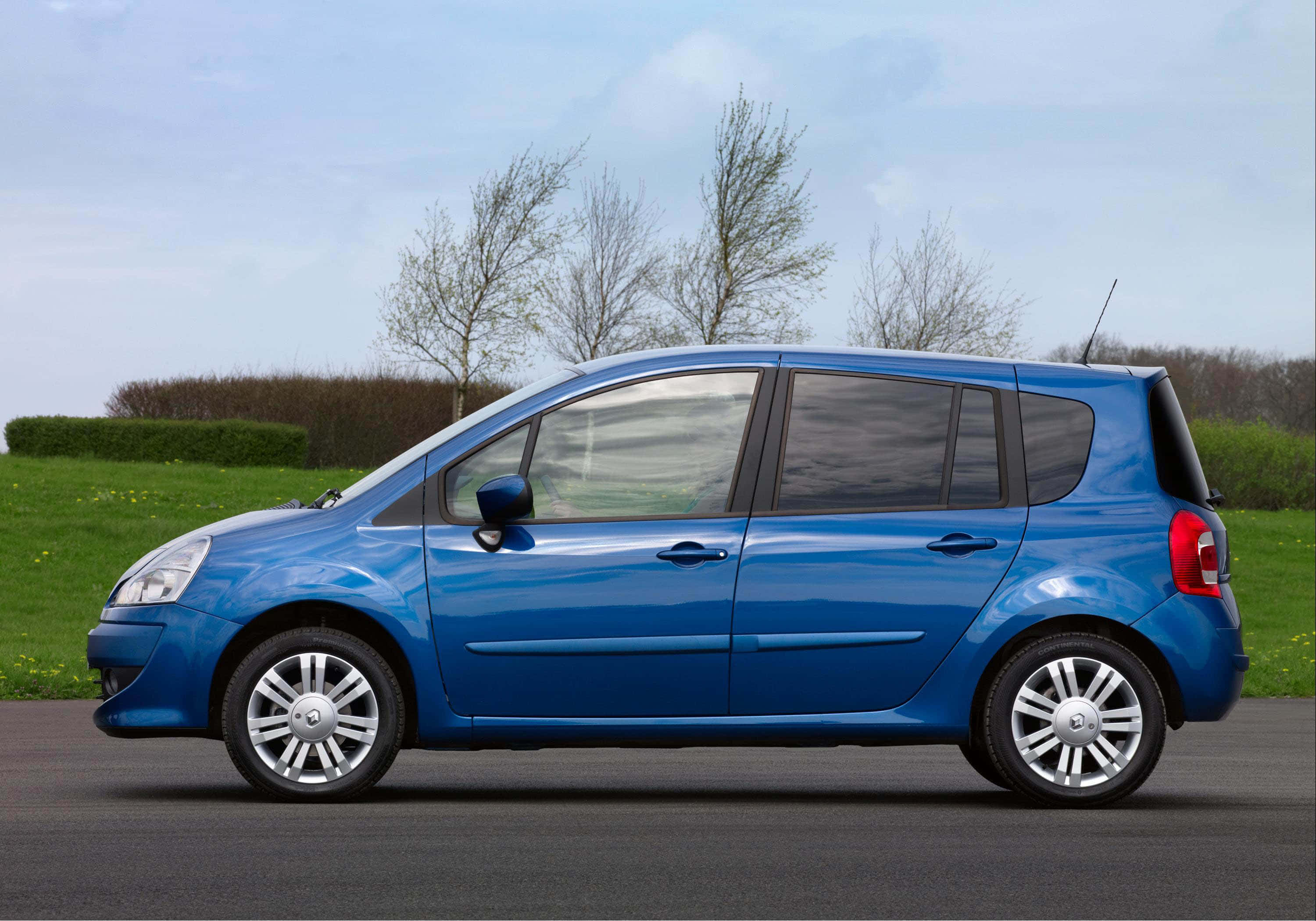 Renault Modus 桌布 壁紙 — 一輛鮮藍色的雷諾 Grand Scenic 小型貨車停在瀝青路上，周圍有光禿禿的樹木和綠草，天空蒼白。