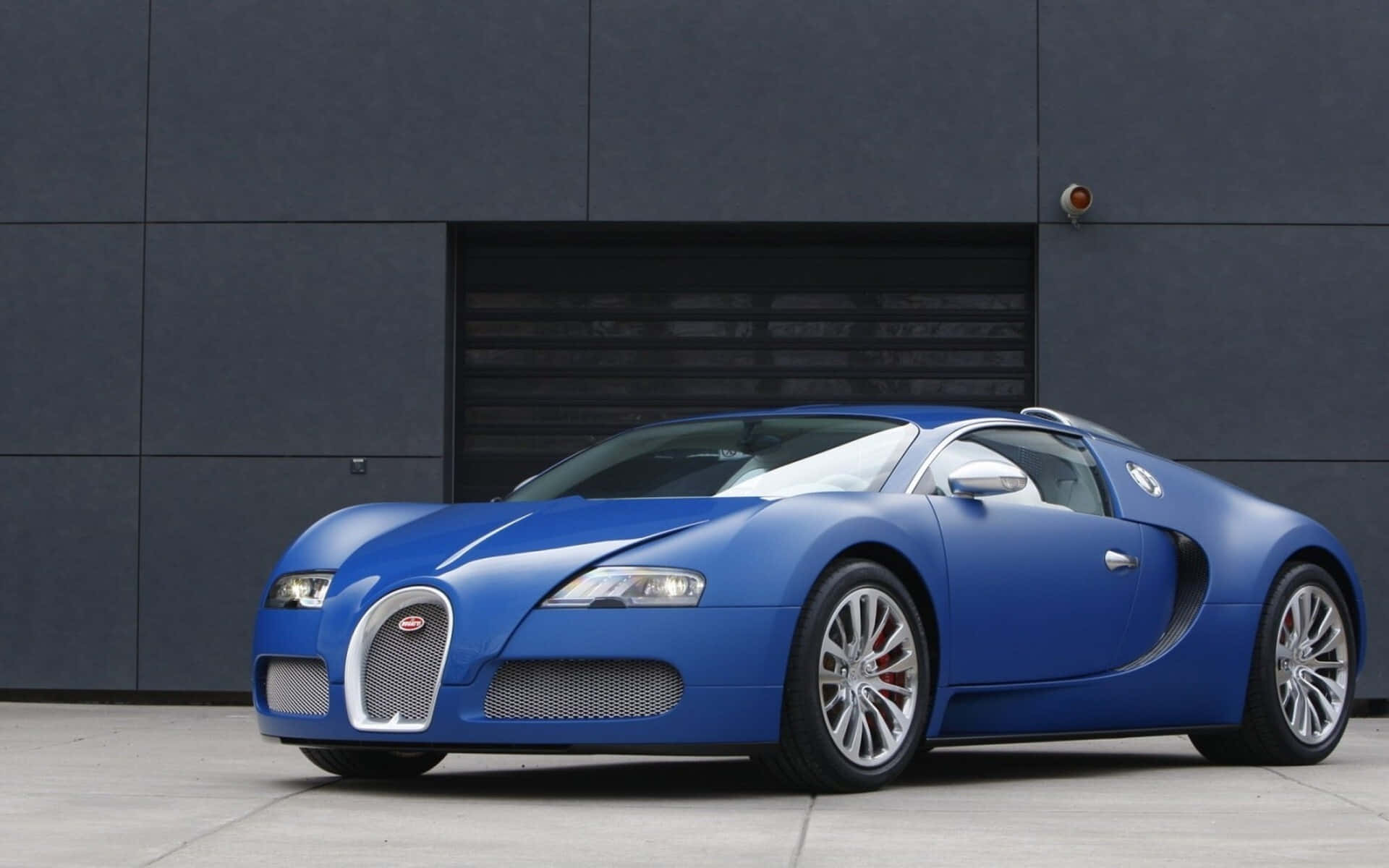 Bugatti Veyron 桌布 壁紙 — 一輛引人注目的藍色Bugatti Veyron跑車停在時尚的深灰色工業建築前。