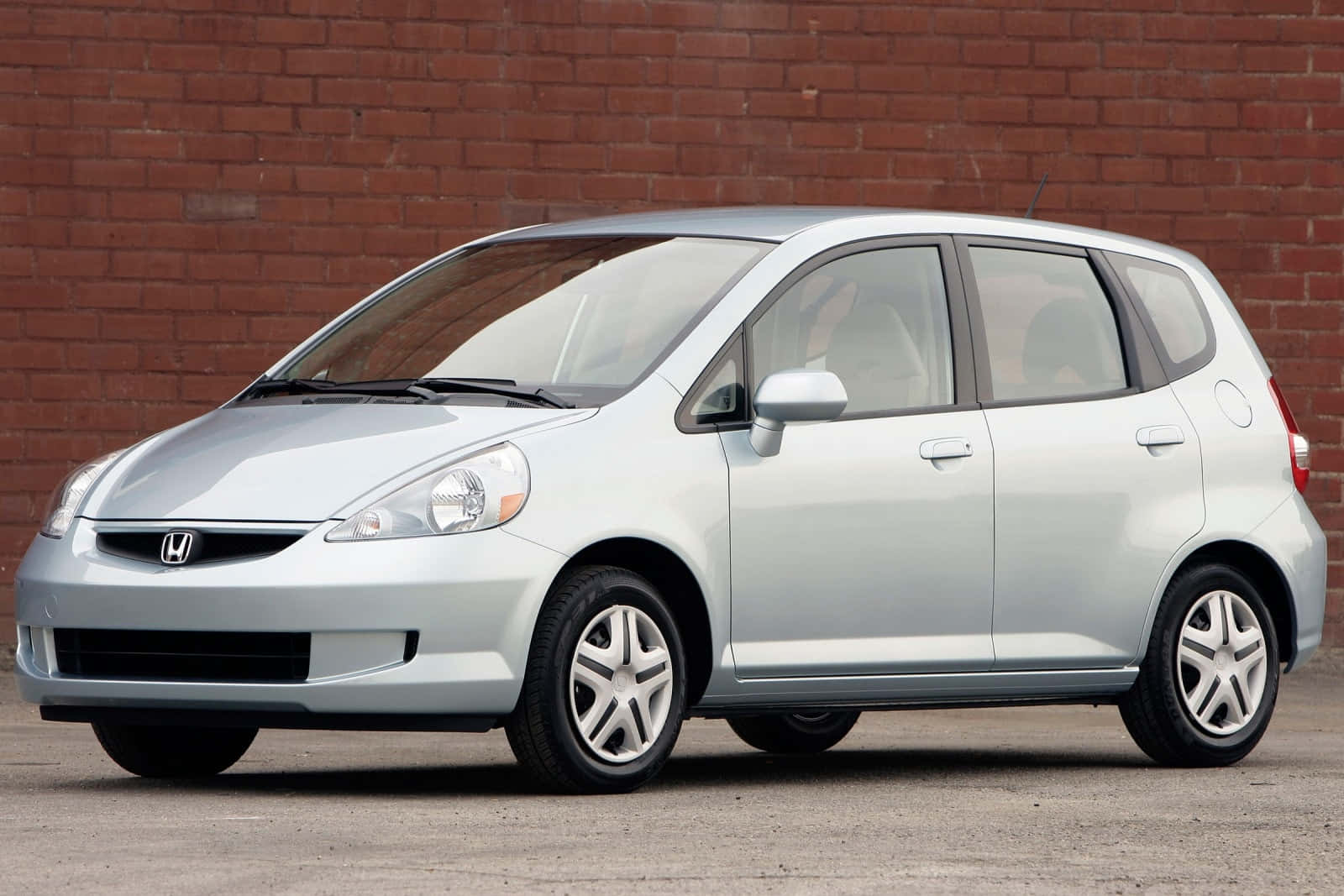 Honda Fit 桌布 壁紙 — 一輛銀色本田Fit在明亮的日光下停泊在紅磚牆旁的鋪砌地面上。