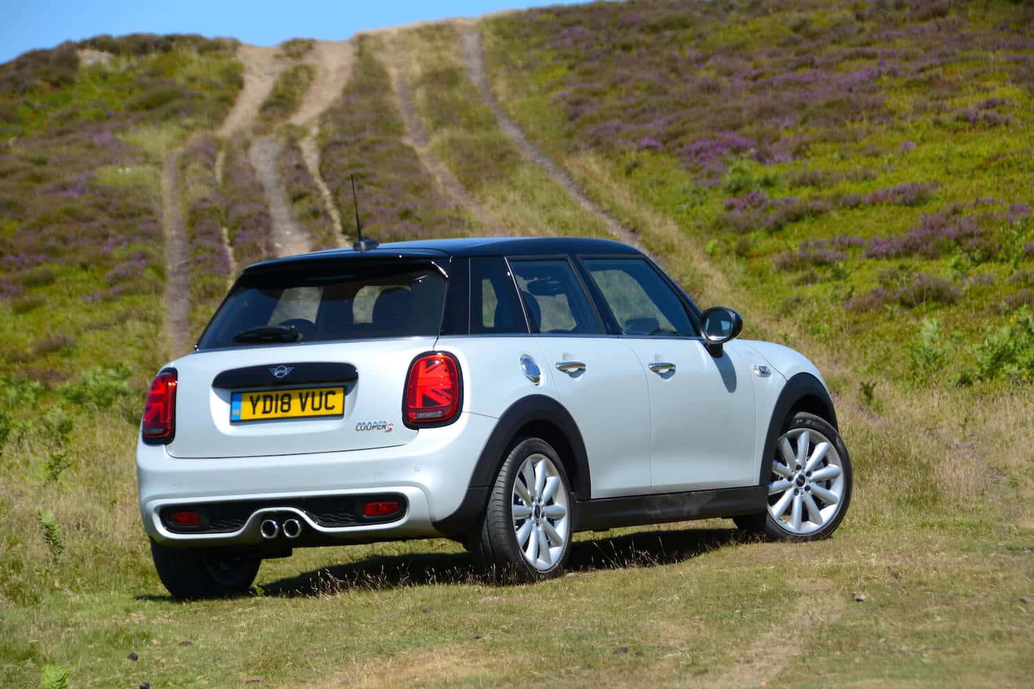 Mini Cooper S 桌布 壁紙 — 一輛銀色MINI Cooper停泊在陽光普照的山坡草地上，周圍有紫色石楠花和泥路。