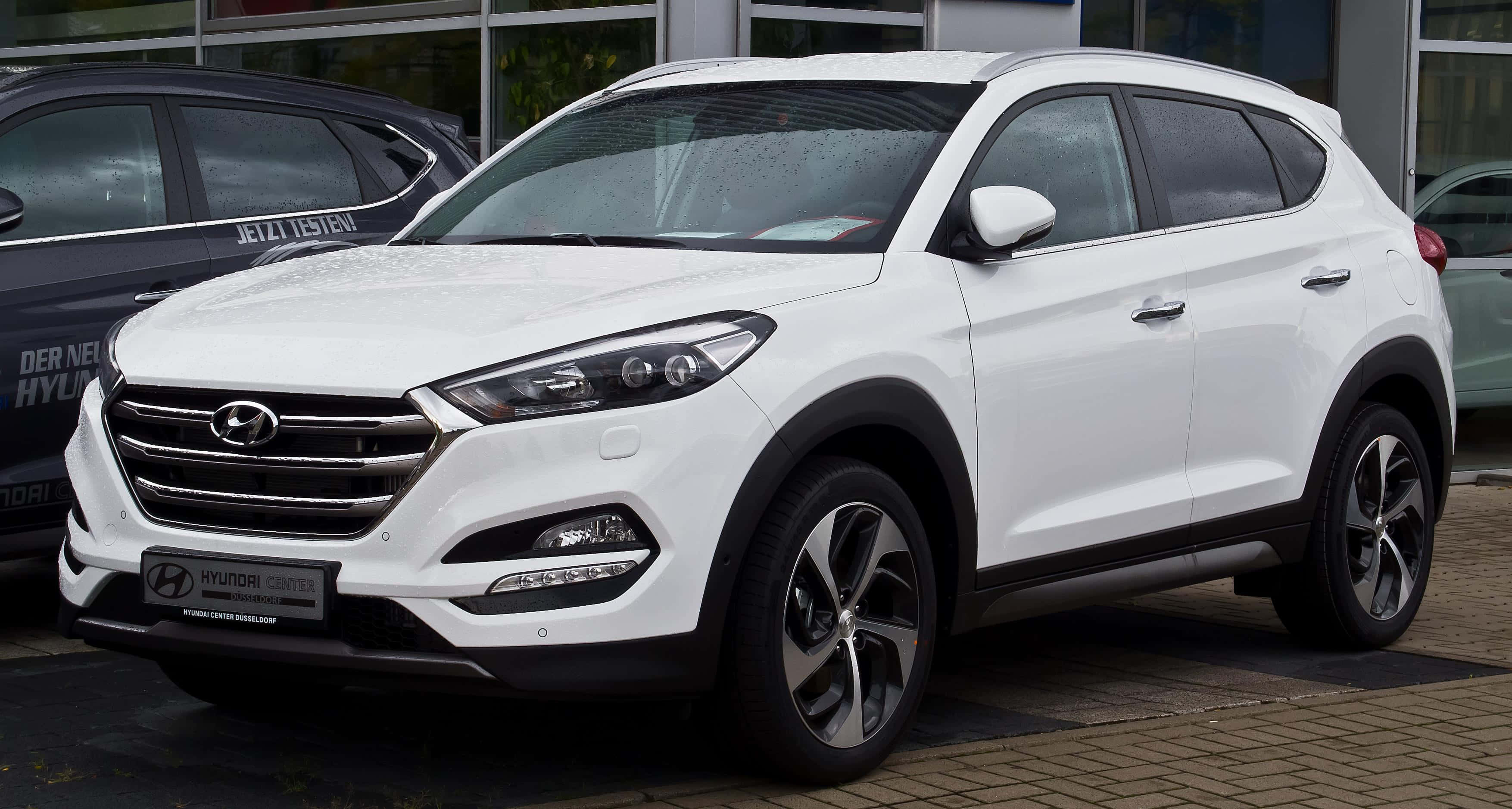Hyundai Tucson 桌布 壁紙 — 一輛純白色的現代Tucson SUV停泊在磚砌車道上，前方是玻璃窗的經銷商。