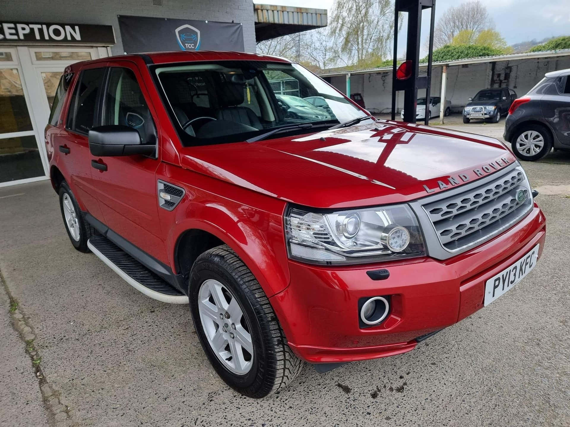 Land Rover Freelander 桌布 壁紙 — 一輛光亮的紅色 Land Rover Freelander 停泊在經銷商外，背景可見其他車輛。