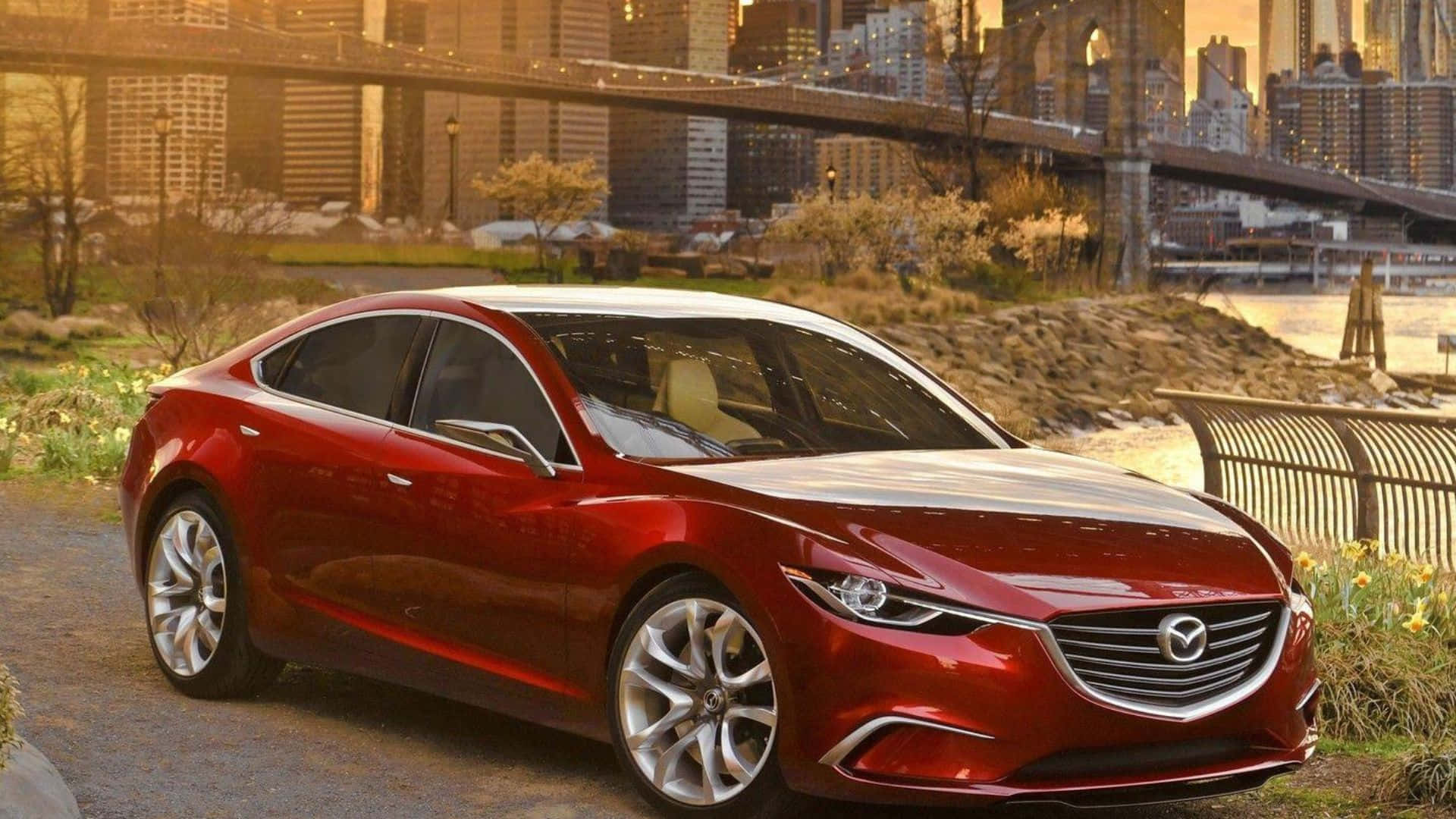 Mazda 6 桌布 壁紙 — 一輛光亮的紅色萬事得房車停泊在河邊，城市橋樑和天際線在黃金時段的光芒中閃耀。