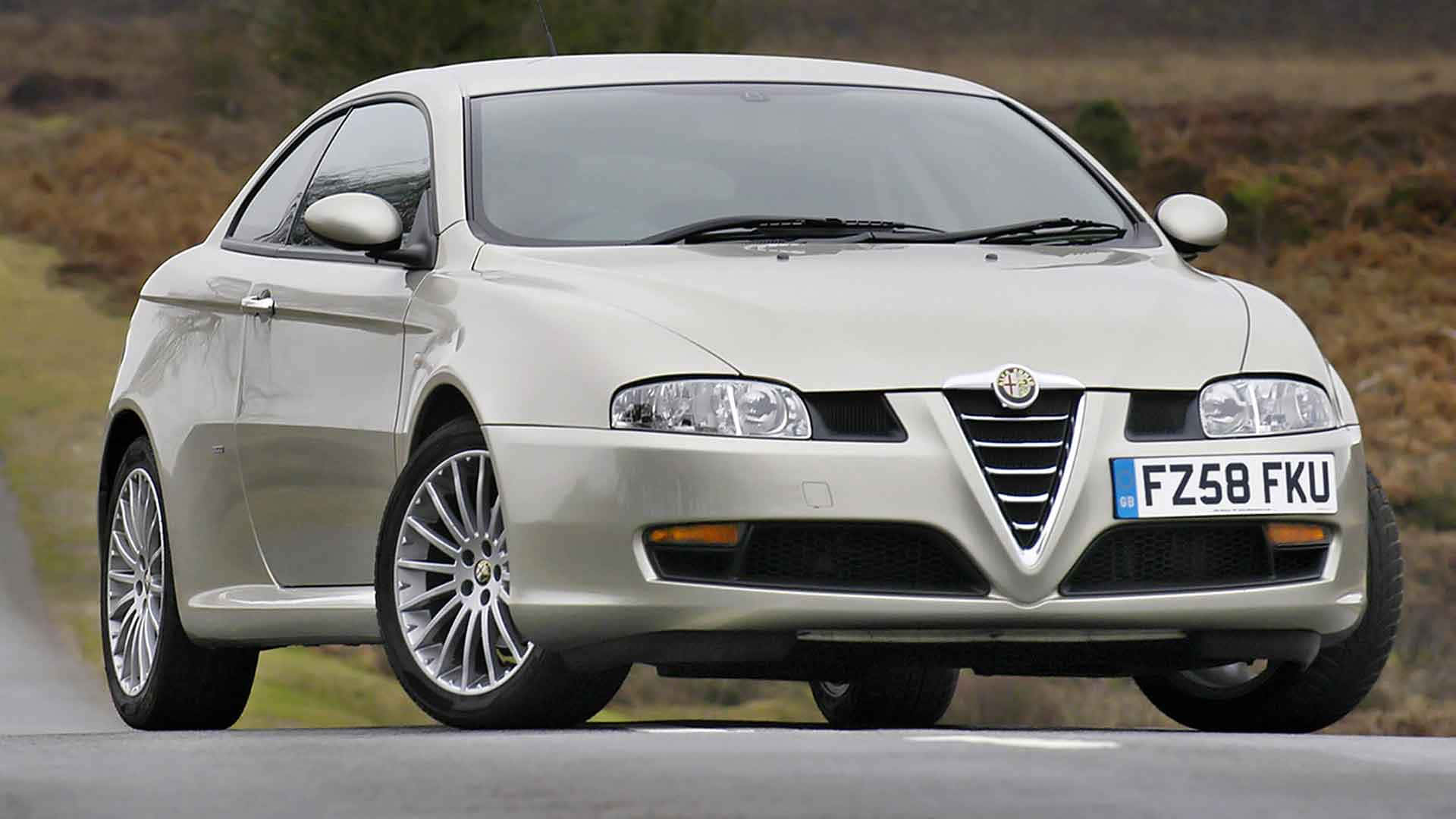 Alfa Romeo Gt 桌布 壁紙 — 一輛銀色愛快羅密歐轎跑車在鄉村道路上行駛，背景是模糊的草坡。