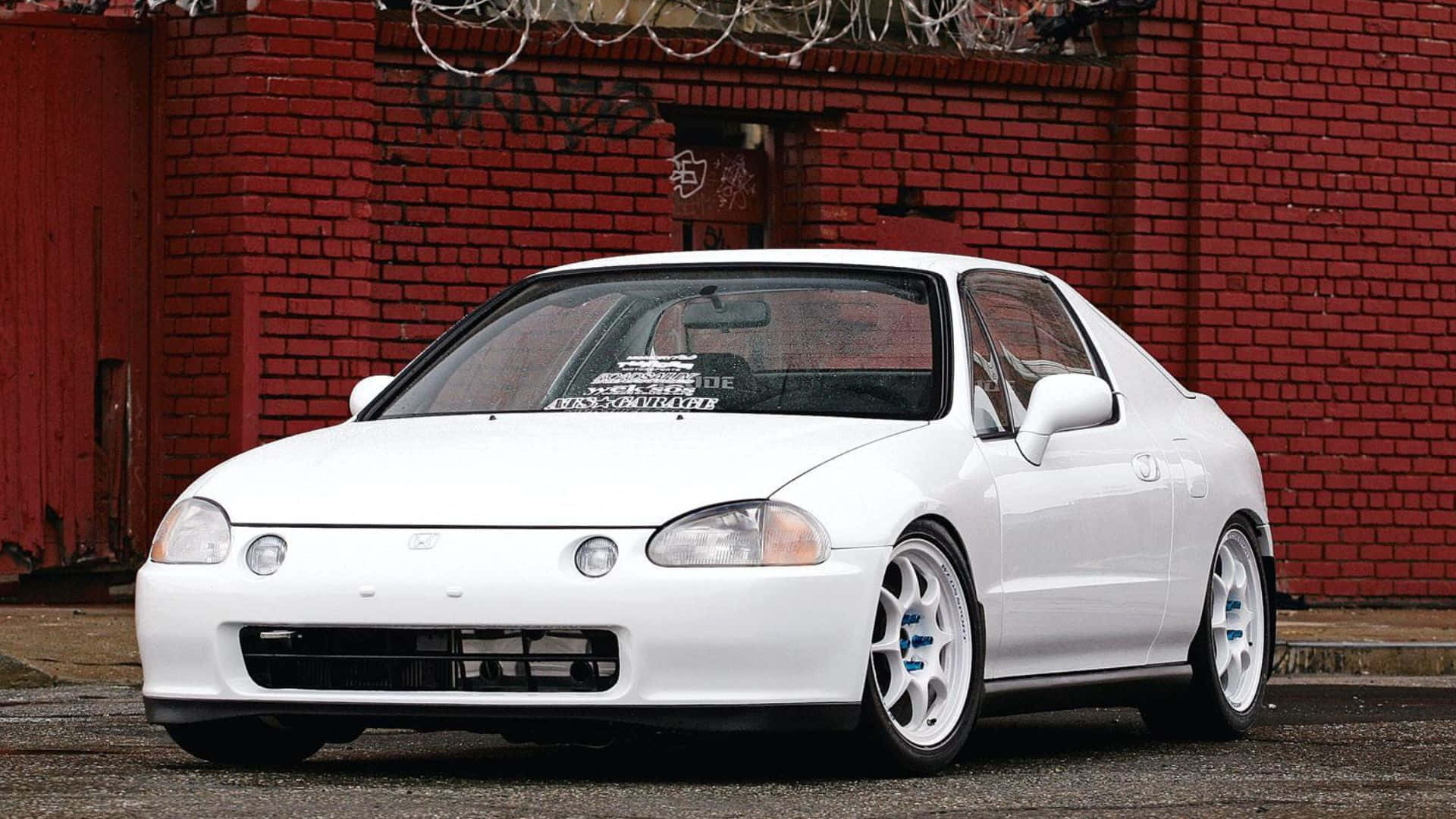 Honda Civic Del Sol 桌布 壁紙 — 一輛純白色的本田思域雙門轎跑車，配備訂製輪圈，停放在一條頂部有鐵絲網的風化紅磚牆前。