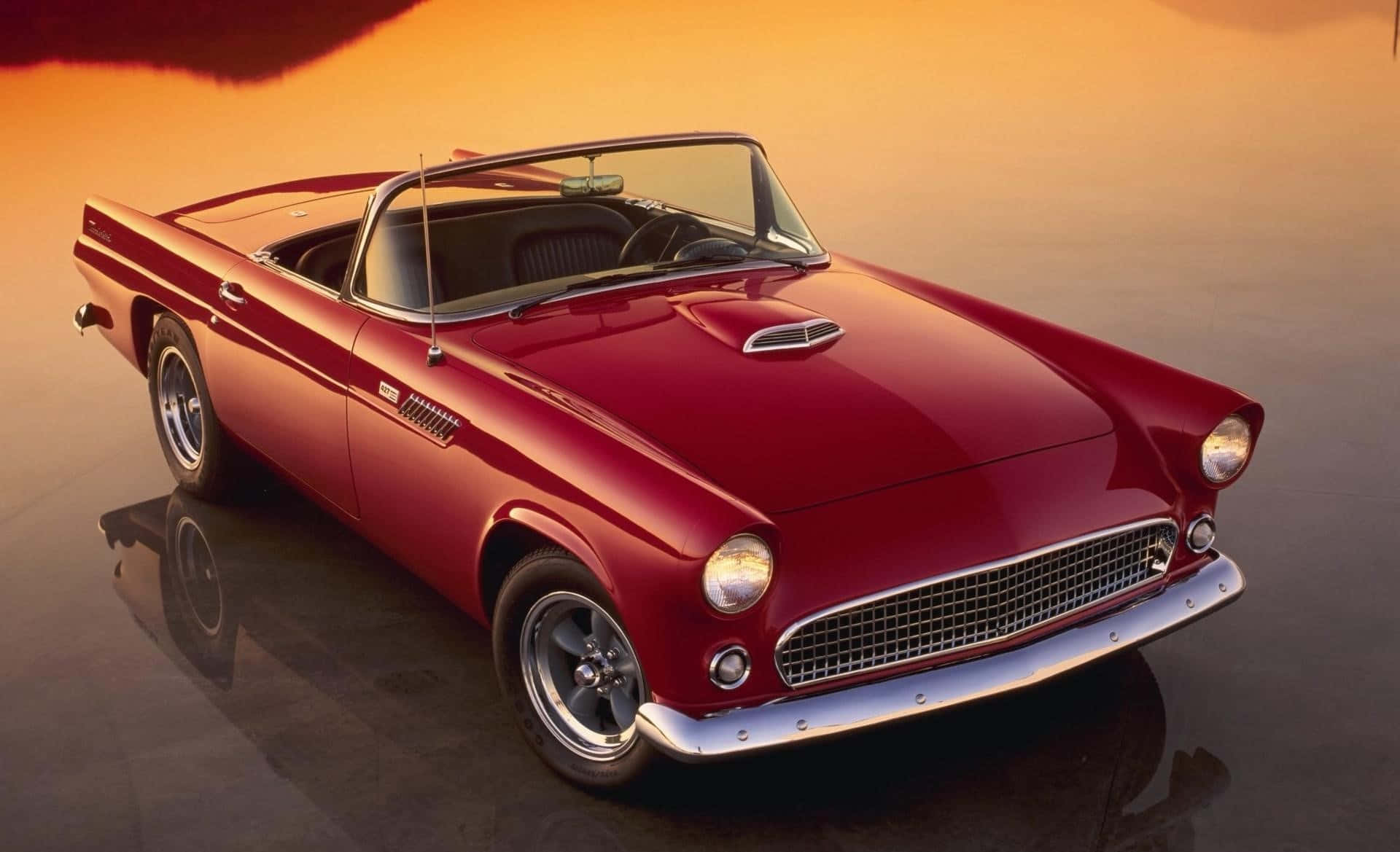 Ford Thunderbird 桌布 壁紙 — 一輛光澤的紅色經典敞篷跑車在溫暖的夕陽光下，在反光的濕滑表面上閃閃發光。