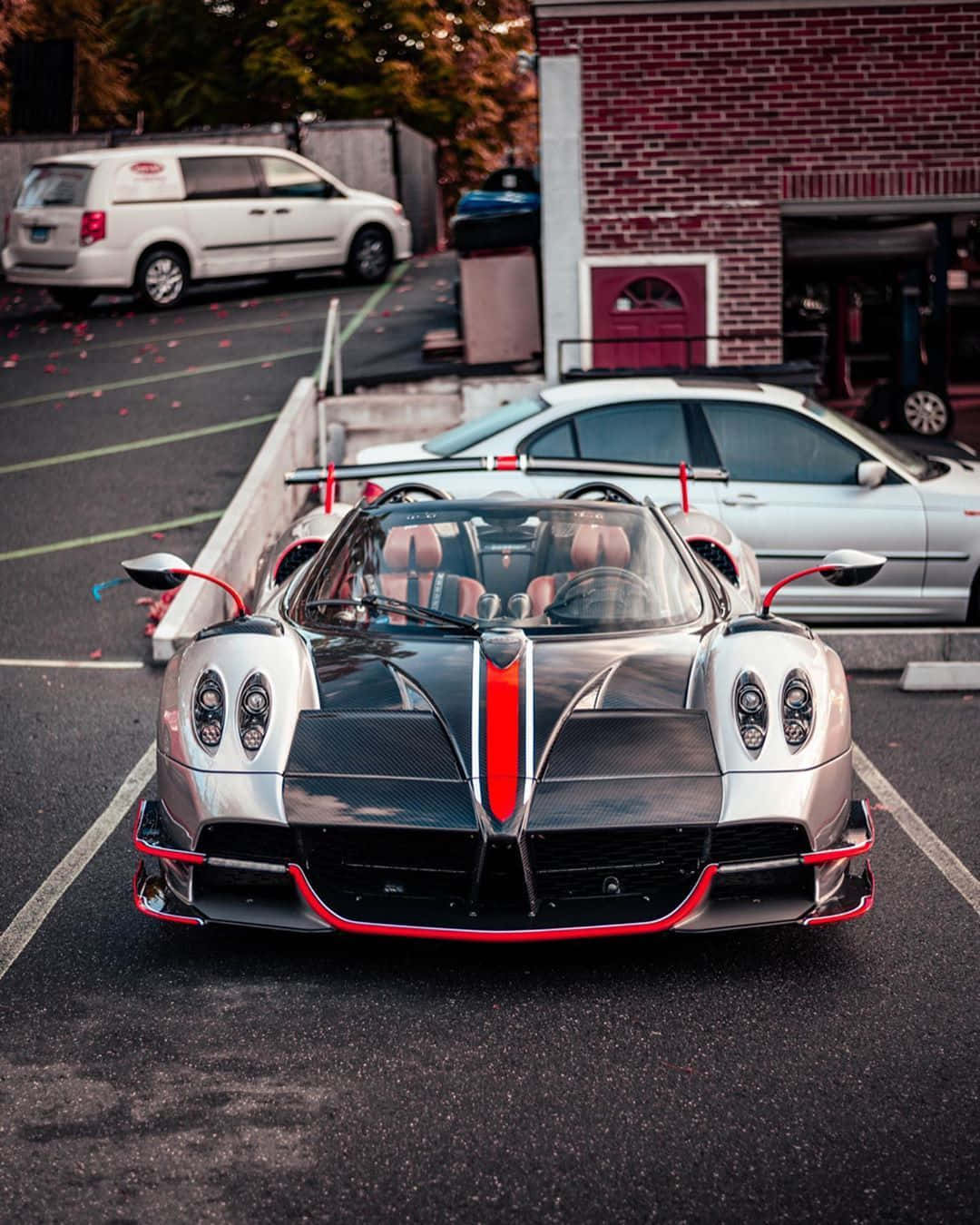 Pagani Huayra Roadster Bc 桌布 壁紙 — 一輛銀黑色帕加尼Huayra帶紅色點綴停泊在瀝青停車場，旁邊是磚砌建築。