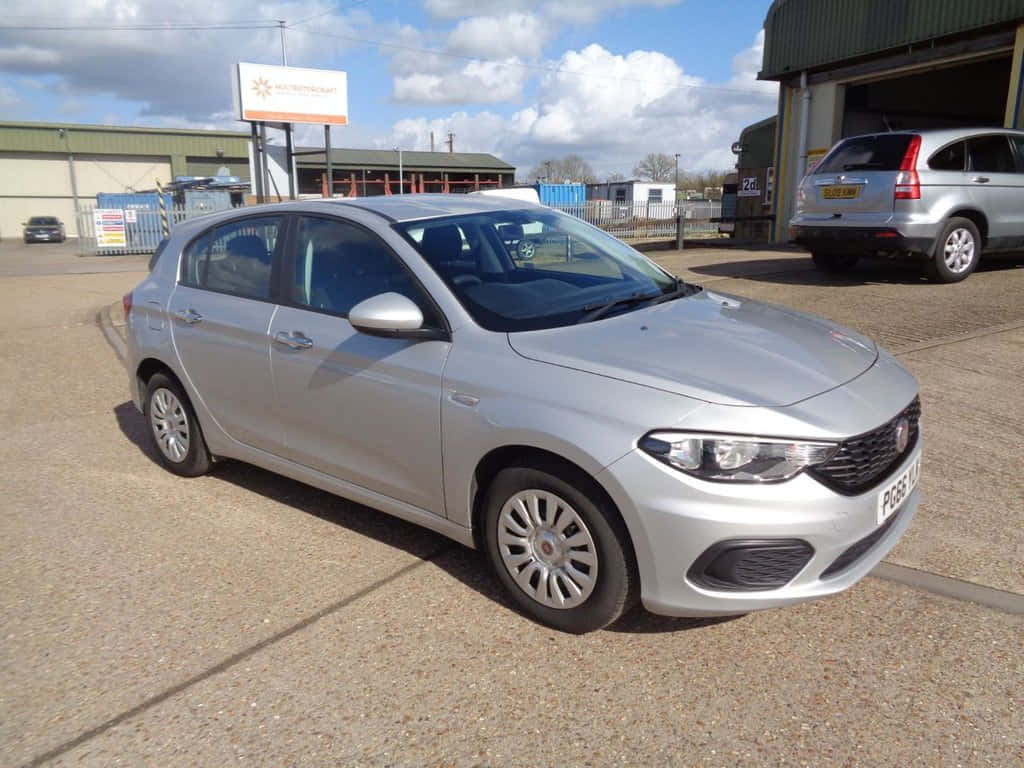 Fiat Tipo 桌布 壁紙 — 一輛銀色 Fiat Punto 停泊在經銷商場地的碎石上，天空局部多雲。