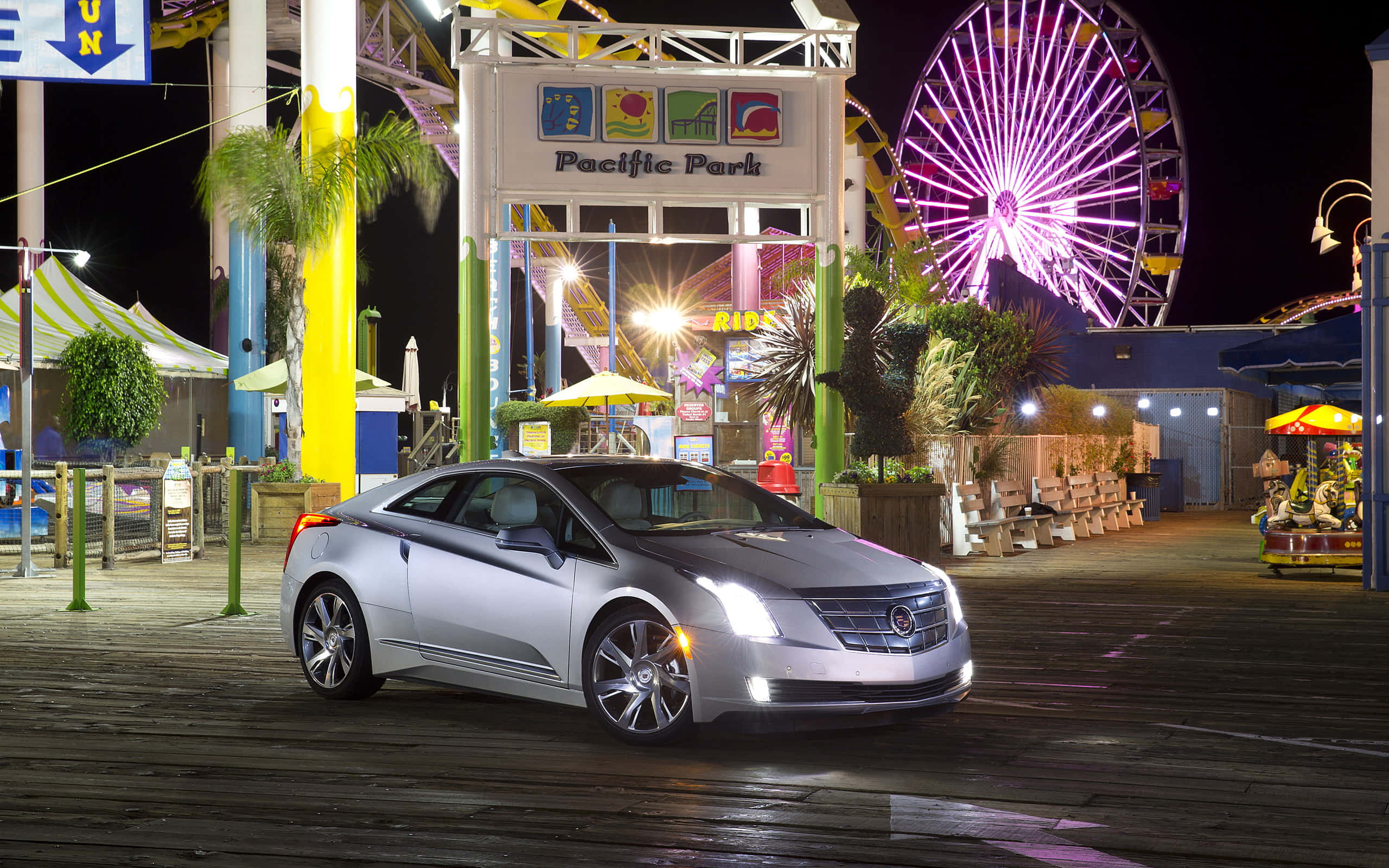 Cadillac Elr 桌布 壁紙 — 一輛銀色凱迪拉克雙門跑車在夜間太平洋公園遊樂碼頭的霓虹燈下閃閃發光，背景有發光的摩天輪。