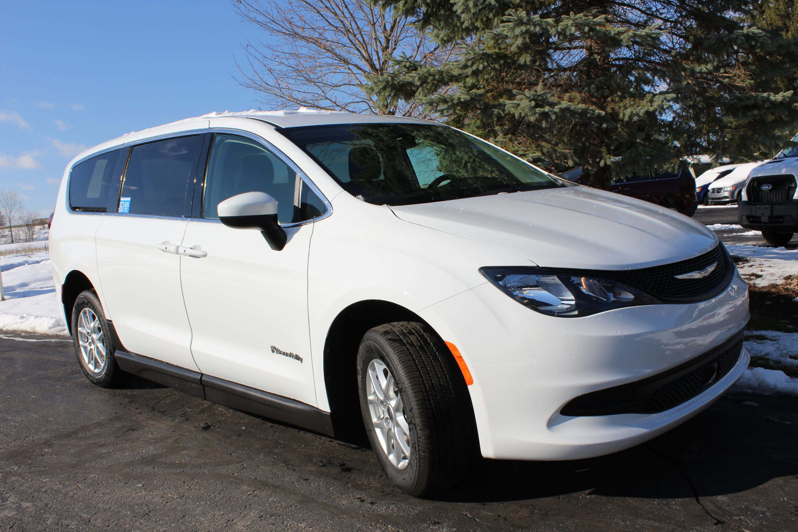 Chrysler Voyager 桌布 壁紙 — 一輛純白色的 Chrysler Pacifica 小型貨車停泊在雪地上，背景是晴朗的藍天和常綠樹。