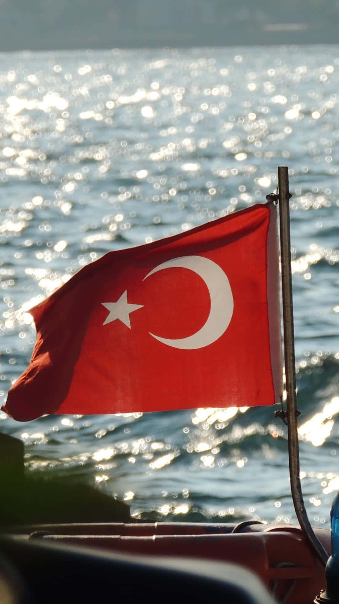 Turkish 桌布 壁紙 — 一面土耳其國旗在船上飄揚，背景是閃爍的陽光海面和地平線上的遠方陸地。