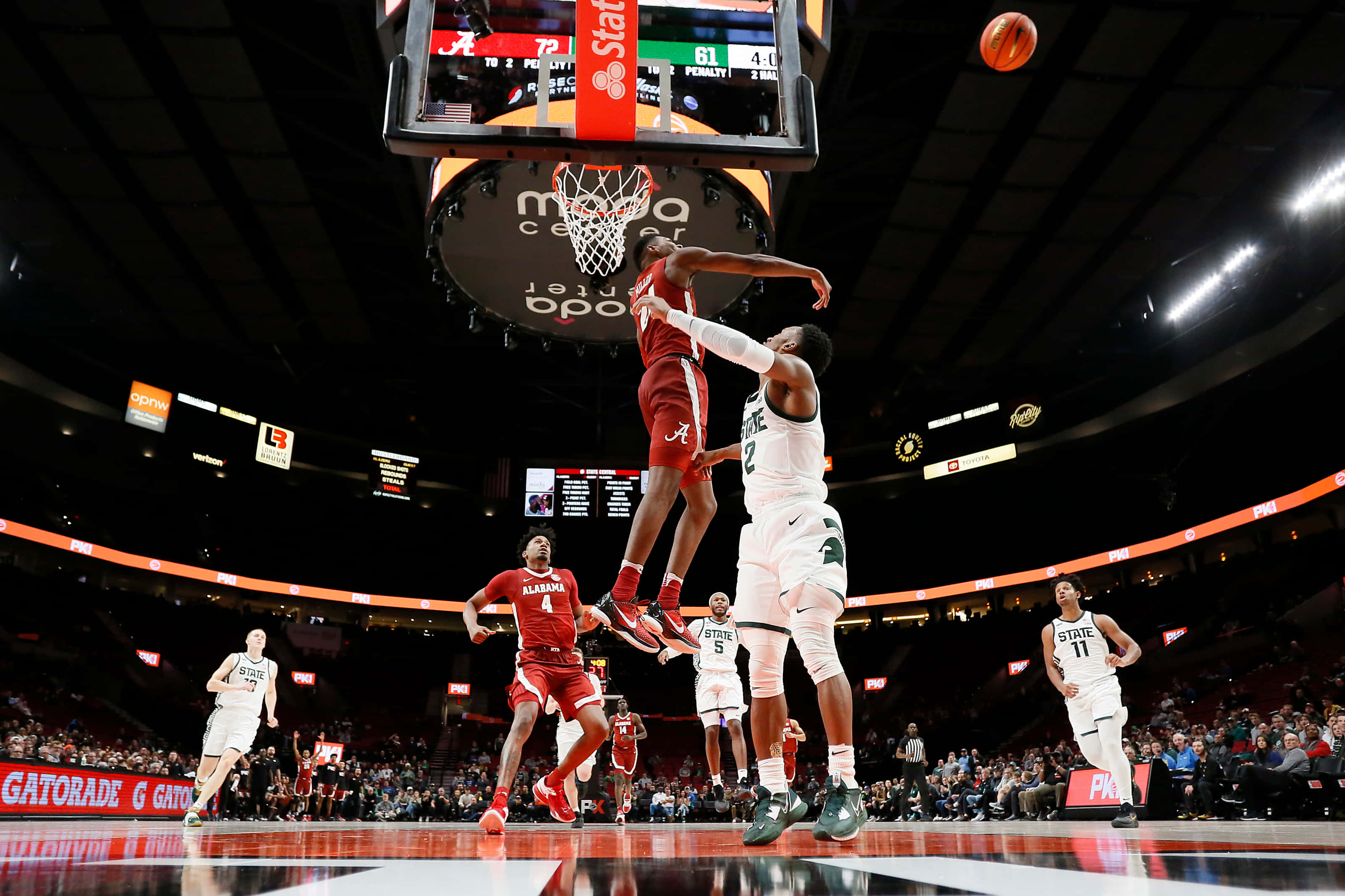 Alabama Basketball 桌布 壁紙 — 一名身穿紅色球衣的籃球運動員跳向籃框，而一名身穿白色球衣的防守球員跳起試圖封阻他的投籃，比賽非常激烈。