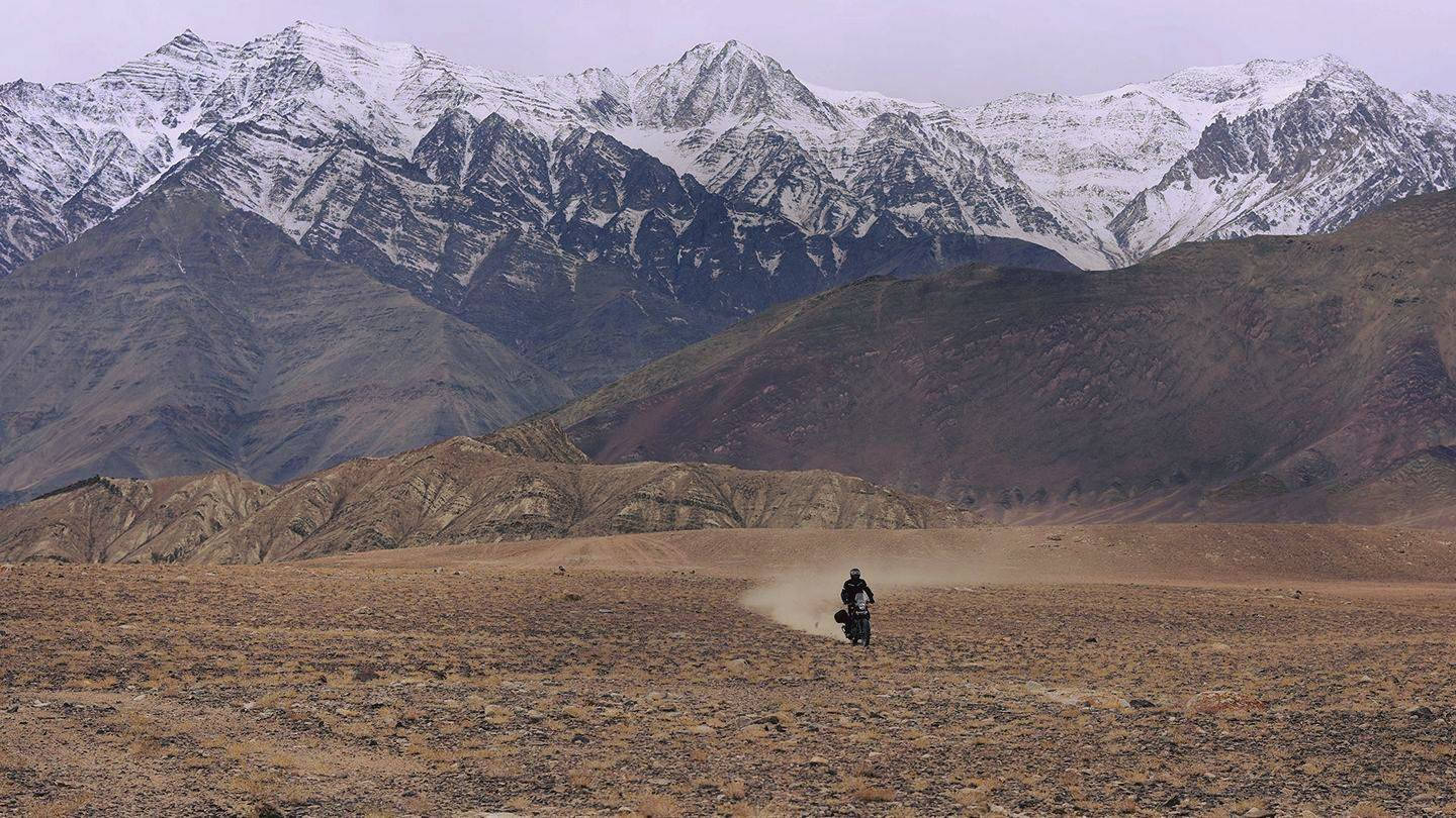 電單車手在沙漠中行駛，背景有雪山