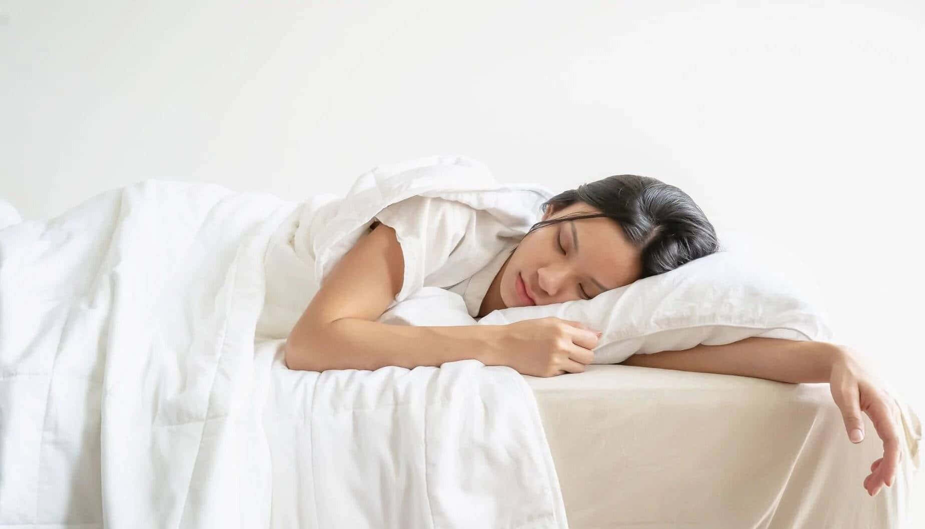  壁紙 — 一名女性在柔軟的白色被子下側臥，在簡約風格的臥室中安詳入睡，明亮自然光灑入。