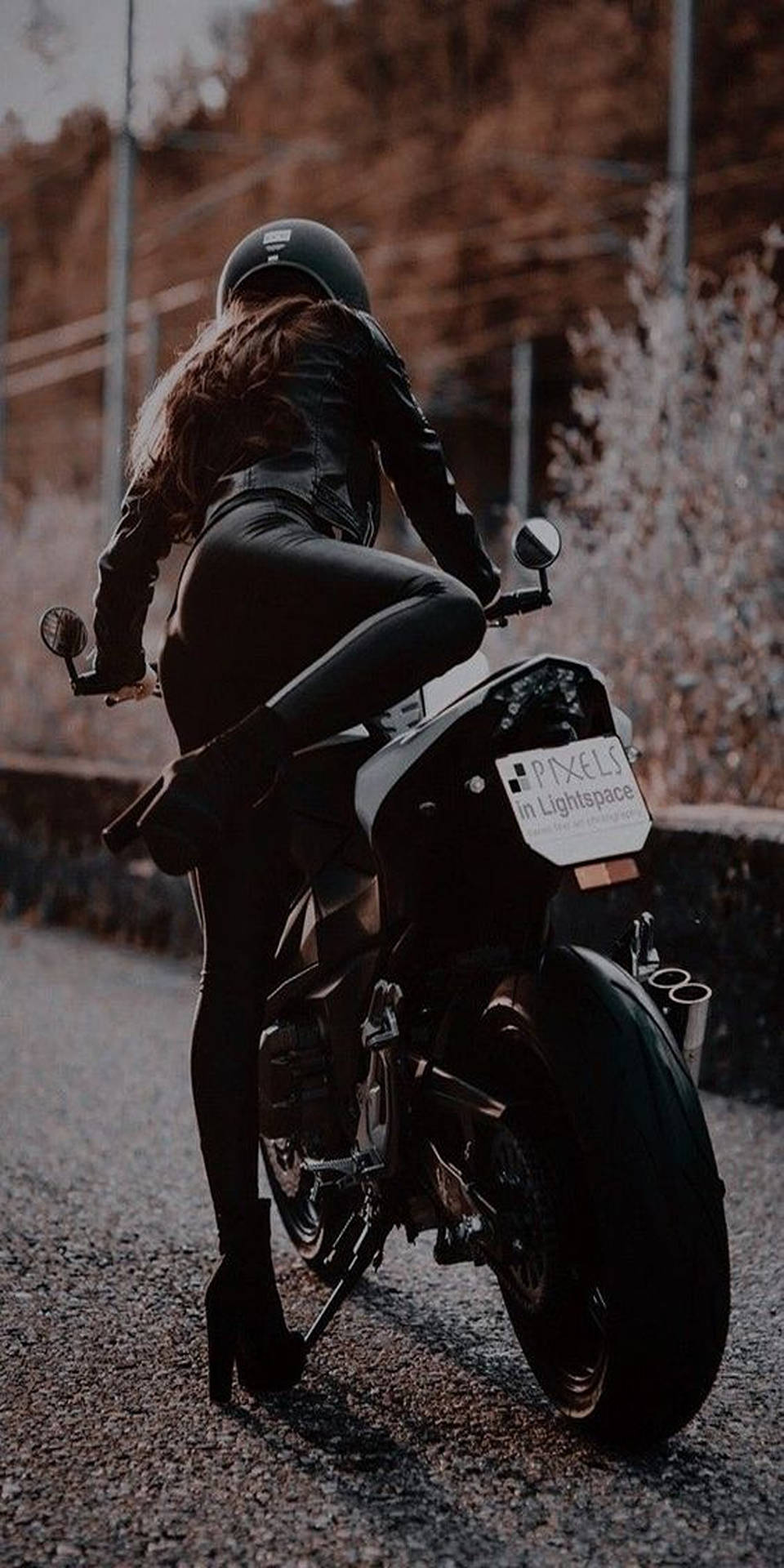 身穿黑色皮革的女性在日落時分騎電單車在碎石路上