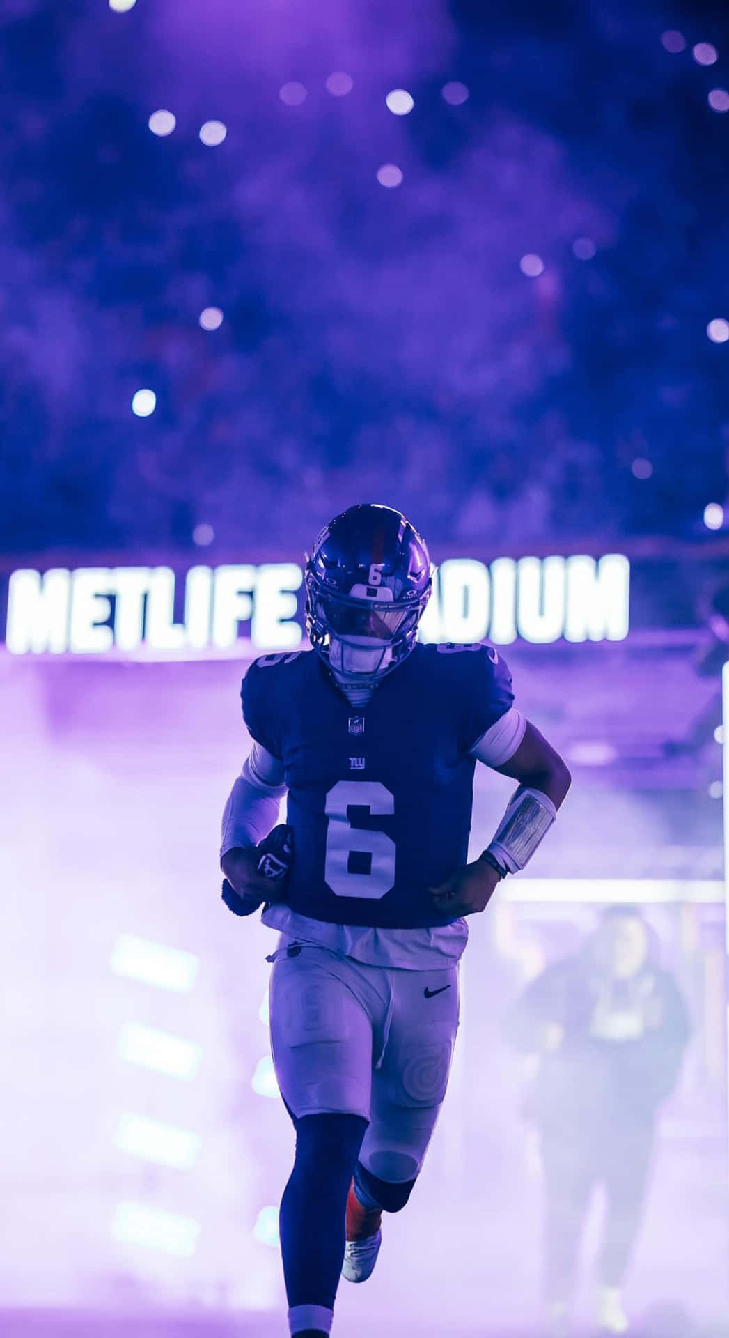  壁紙 — 一名身穿6號球衣的美式足球員在MetLife Stadium的球場燈光下穿過紫色煙霧奔跑。