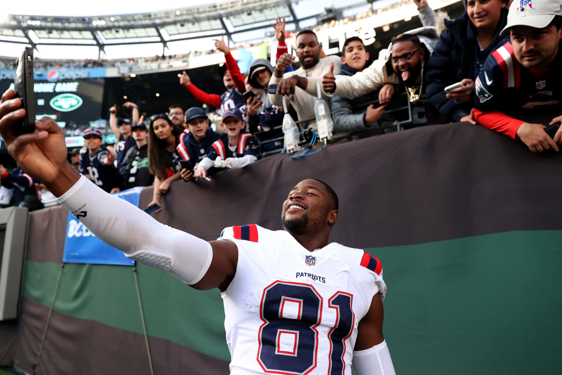 身穿愛國者隊球衣的NFL球員在體育館與歡呼的粉絲自拍。