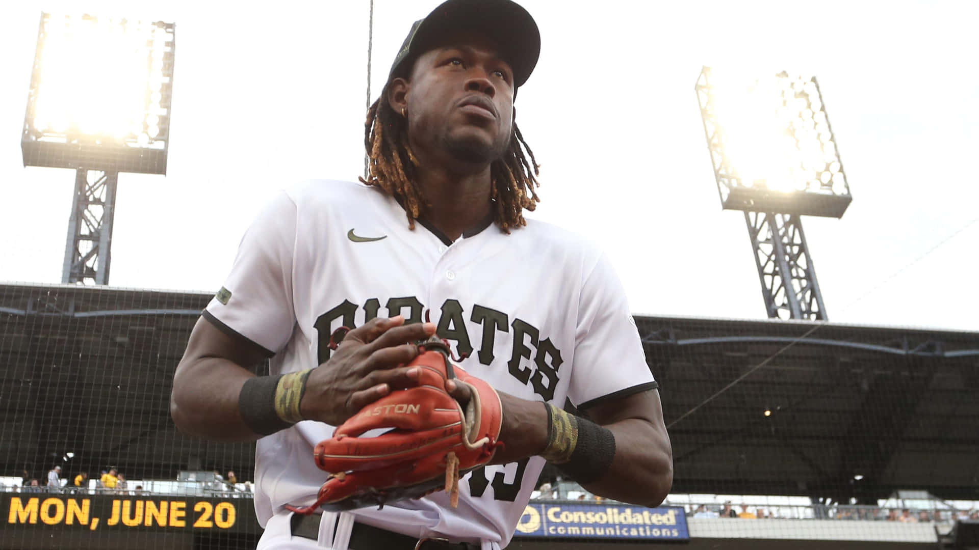  壁紙 — 一名身穿白色 Pirates 球衣的棒球選手，手持紅色手套，站在陽光普照的球場上，身後球場燈光閃爍。