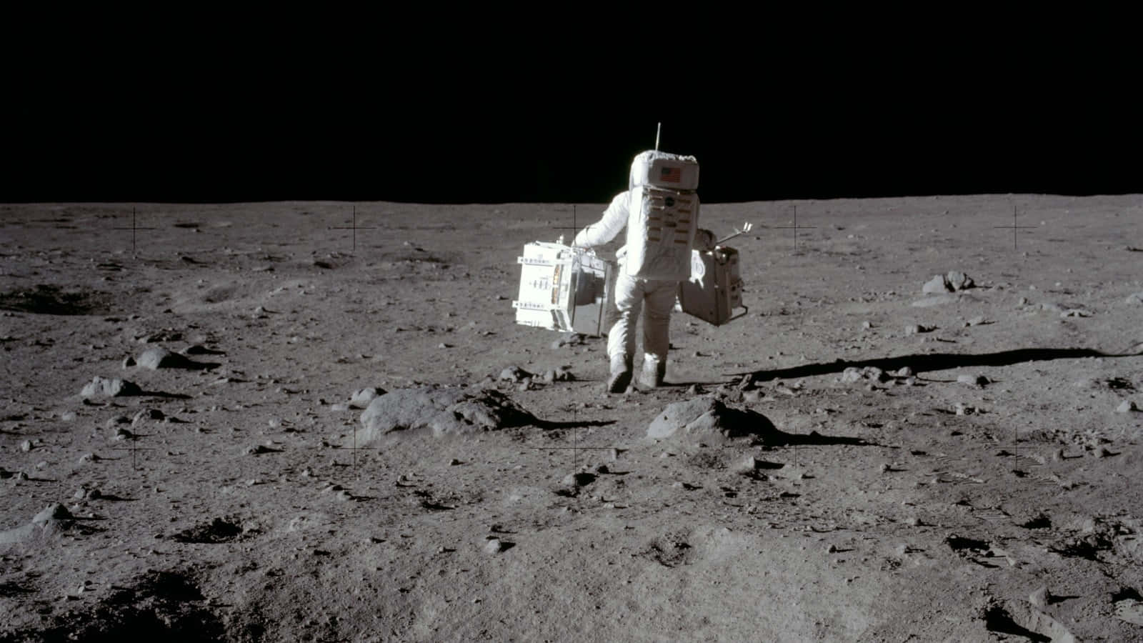 Neil Armstrong 桌布 壁紙 — 一名身穿白色太空衣的太空人在黑色天空下，攜帶設備走過荒蕪的灰色月球表面。