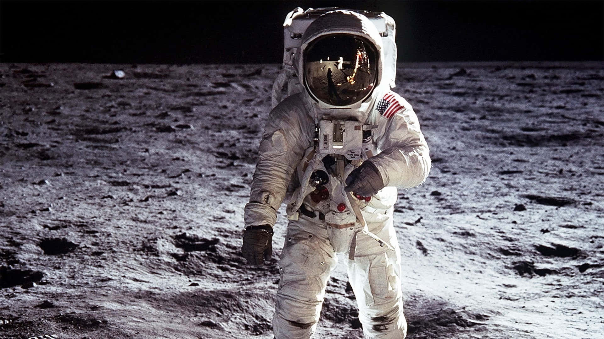 Astronaut On Moon 桌布 壁紙 — 一名身穿白色太空衣的太空人站在月球灰色的隕石坑表面，背景是黑色的天空。