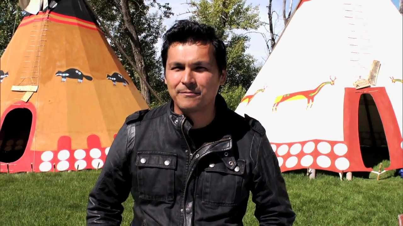  壁紙 — 一名身穿黑色皮褸的男子自信地站在兩個色彩鮮豔的印第安帳篷前，背景是晴朗的藍天。