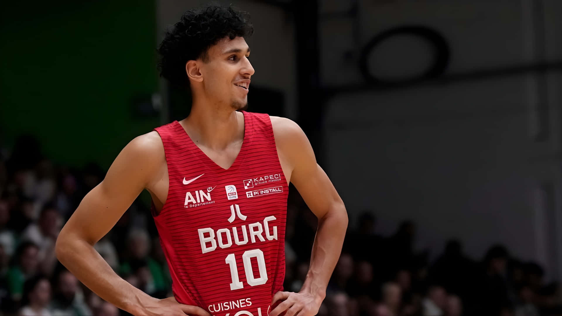  壁紙 — 一名身穿紅色Bourg 10球衣的籃球運動員在比賽中自信地雙手叉腰站立。