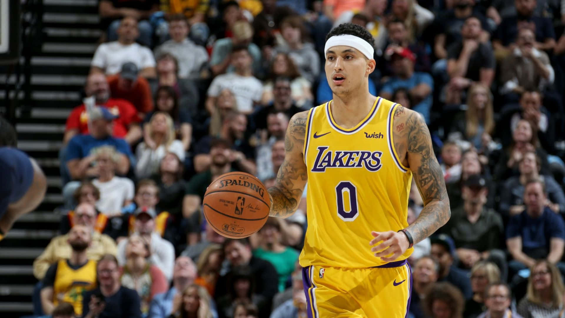  壁紙 — 一名身穿黃色湖人隊球衣的籃球運動員在比賽中運著 Spalding 籃球，背景是模糊的人群。