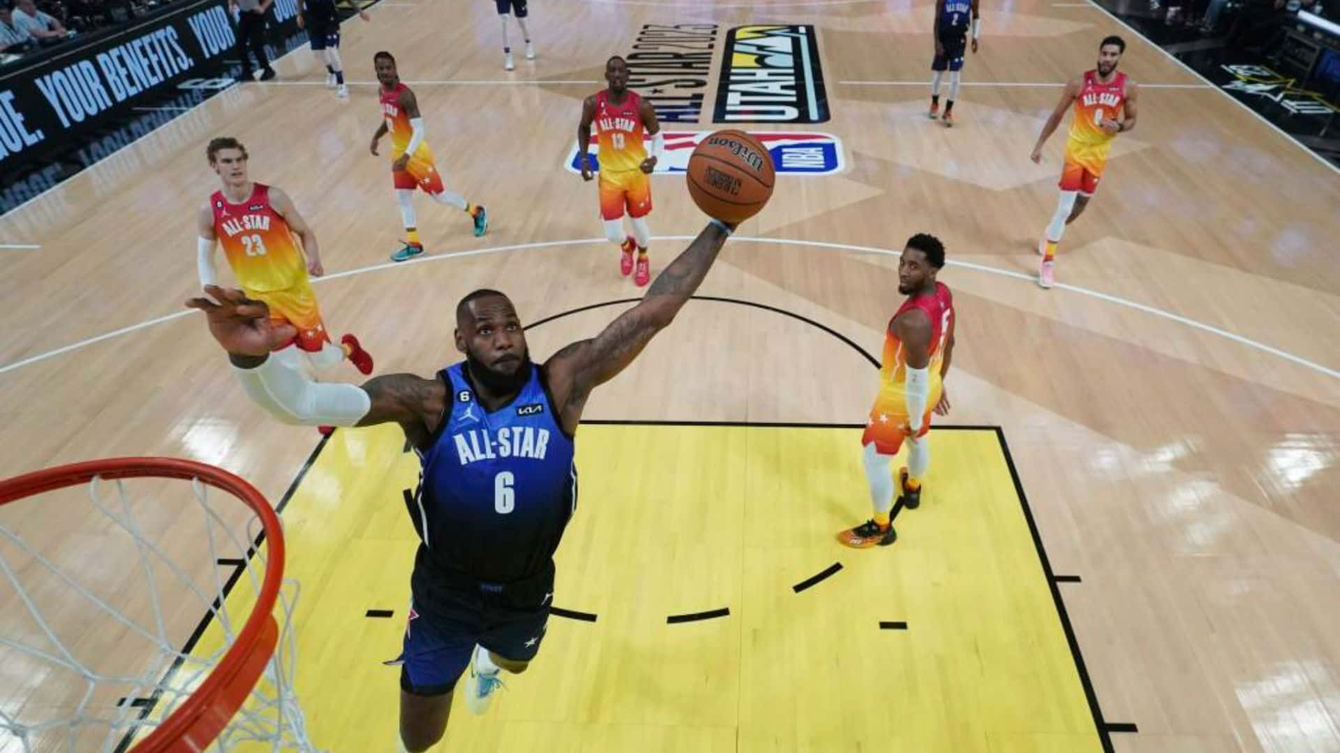 NBA Game 桌布 壁紙 — 一名身穿藍色全明星球衣的籃球運動員在場上大力入樽，身穿橙色球衣的對手在場邊觀看。