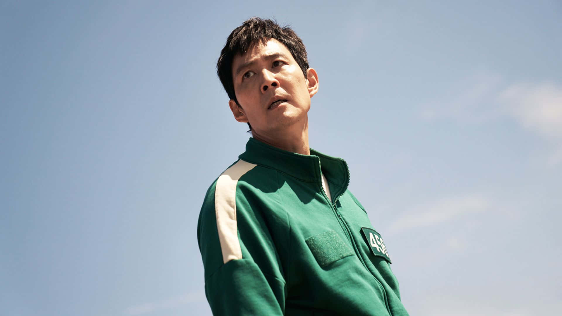  壁紙 — 一名身穿綠色號碼運動服的男子，表情嚴肅地仰望清澈的藍天。