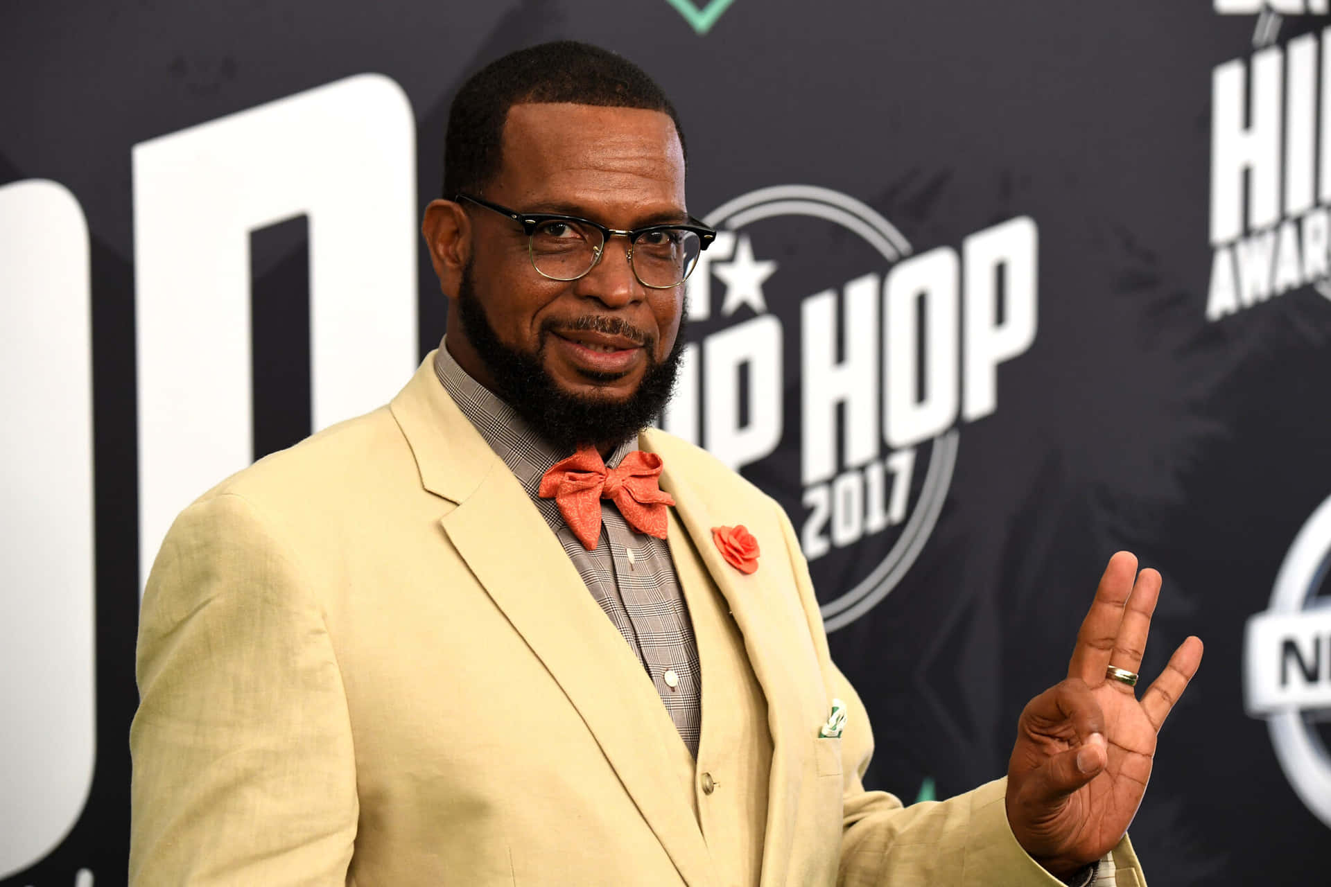  壁紙 — 一名身穿米色西裝及橙色蝴蝶結領帶的男子在2017年Hip Hop Awards上微笑並做出和平手勢。