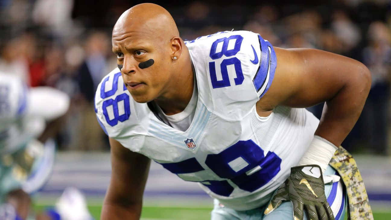  壁紙 — 一名專注的NFL球員身穿白色和藍色制服，在體育場燈光下於足球場上向前傾身。