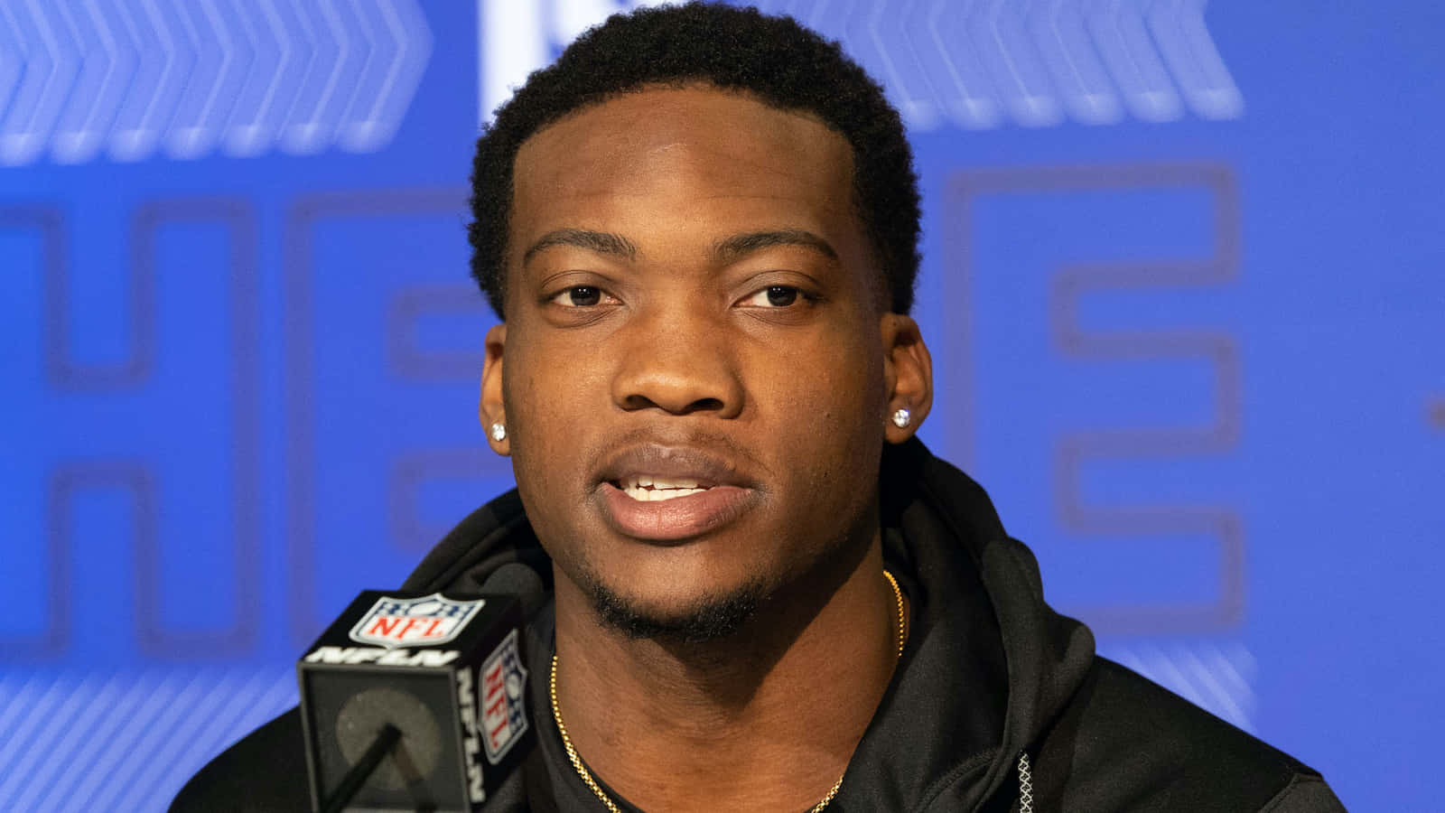  壁紙 — 一名專注的NFL球員在藍色品牌背景的新聞發布會上發言。