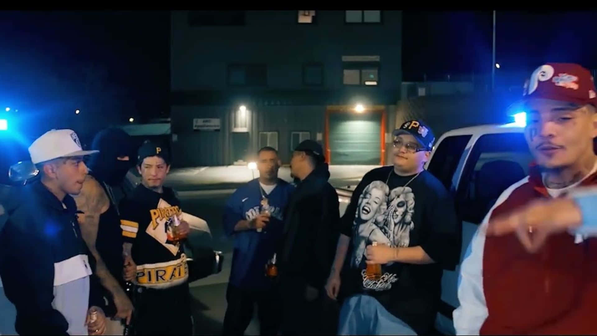  壁紙 — 一群年輕男子在夜晚聚集在一個光線昏暗的城市停車場，靠近一棟建築物和一輛卡車。