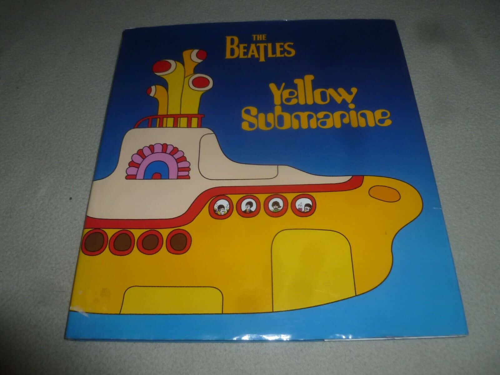 Yellow Submarine 桌布 壁紙 — 一艘充滿活力的黃色潛水艇帶有卡通面孔，漂浮在深藍色天空下的藍色水面上，帶有'The Beatles Yellow Submarine'文字。