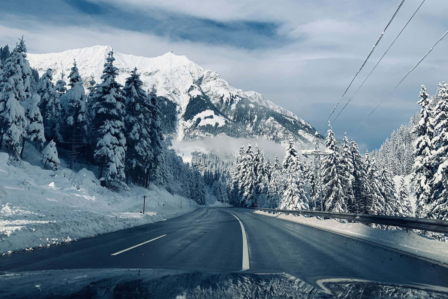 積雪的道路蜿蜒穿過森林，背景有山脈。
