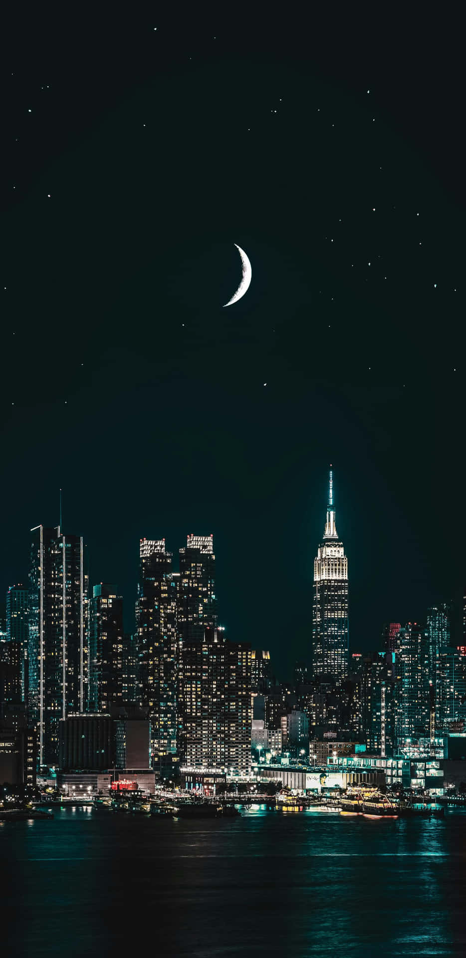  壁紙 — 一彎新月和星星在充滿活力的夜間城市景觀上方閃耀，燈火通明的摩天大樓倒映在水面上。